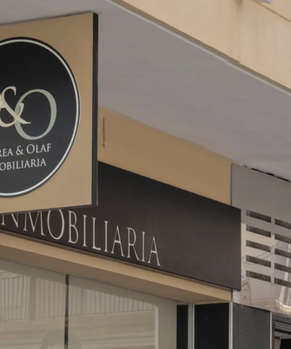 Letrero exterior de la oficina de Andrea & Olaf Inmobiliaria, con logotipo circular sobre fachada de piedra negra y escaparate acristalado.