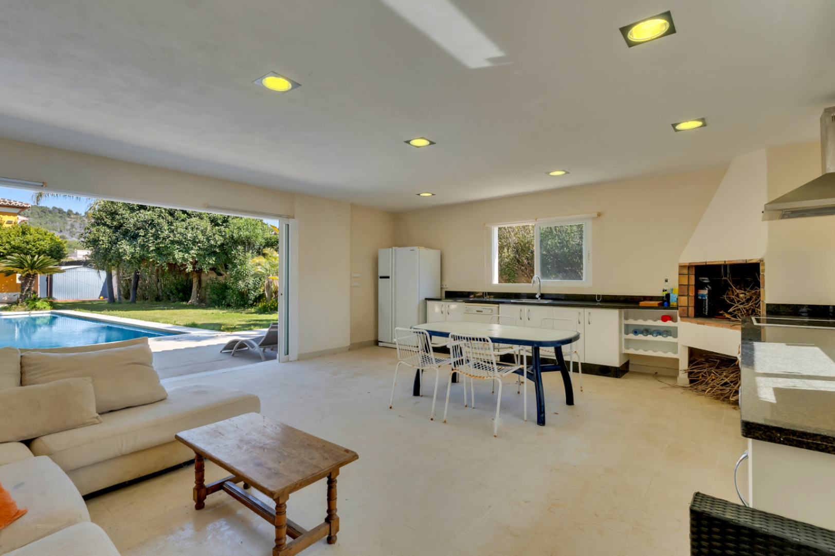 Amplia cocina de verano y zona de estar con barbacoa integrada, conectada directamente a la piscina y al jardín mediante grandes puertas correderas.