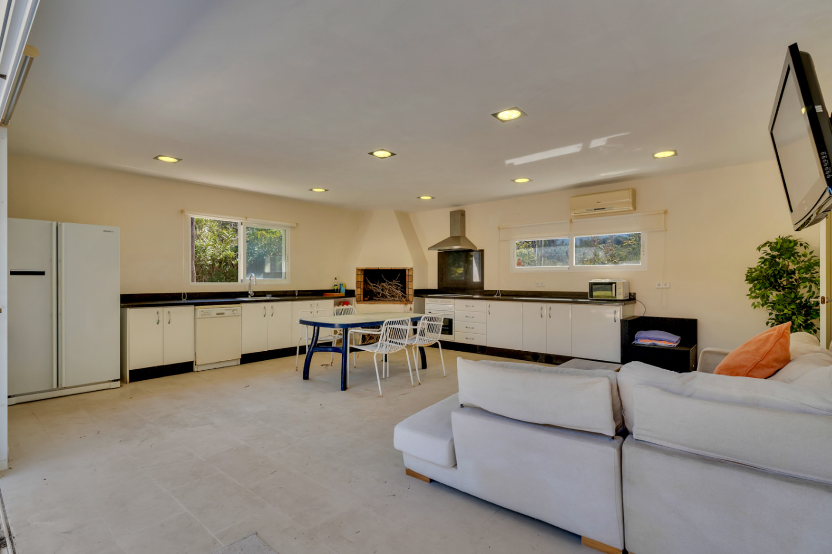 Amplia zona de barbacoa cubierta de 67 m² equipada con cocina completa, chimenea rústica, comedor y sala de estar con aire acondicionado.