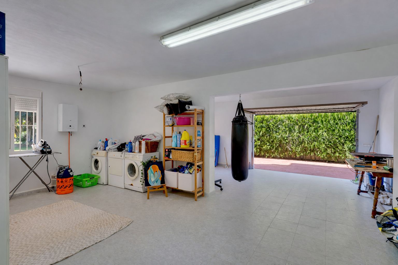 Amplio espacio multifuncional con zona de lavandería, área de gimnasio con saco de boxeo y acceso directo al exterior a través de un gran portón.