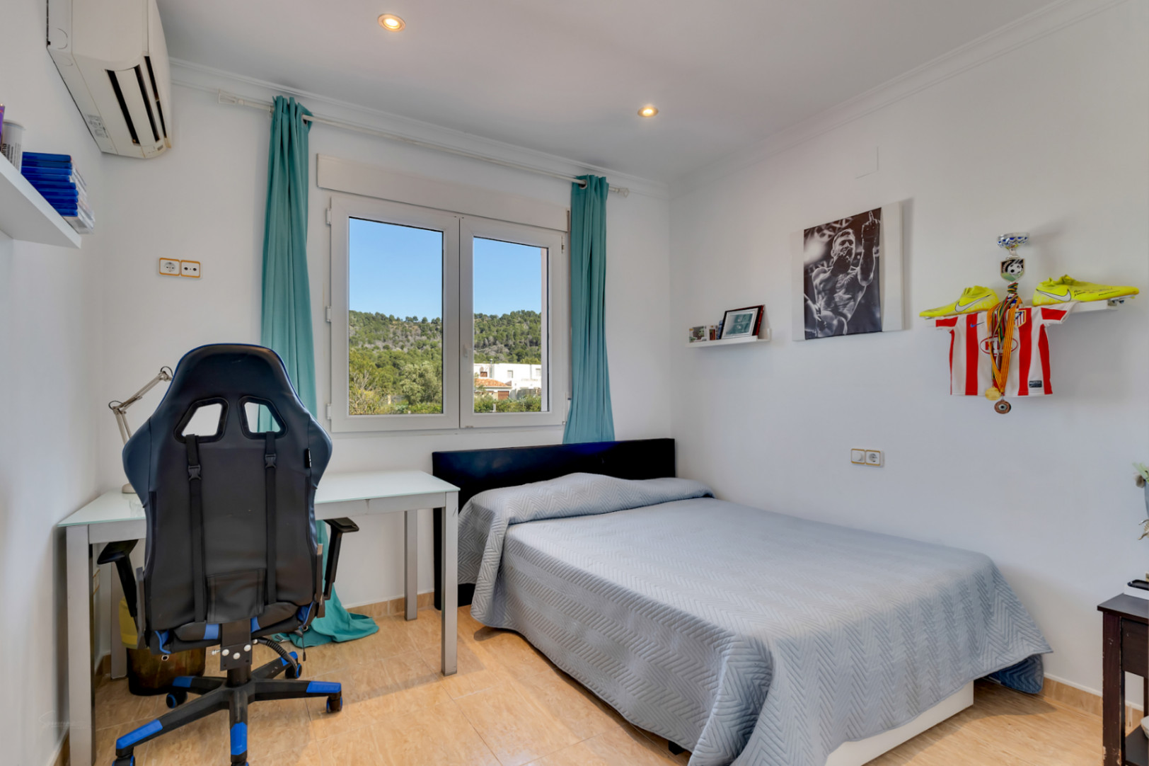 Dormitorio luminoso con zona de estudio, equipado con aire acondicionado, suelos cerámicos y ventana de PVC con vistas despejadas a la naturaleza.
