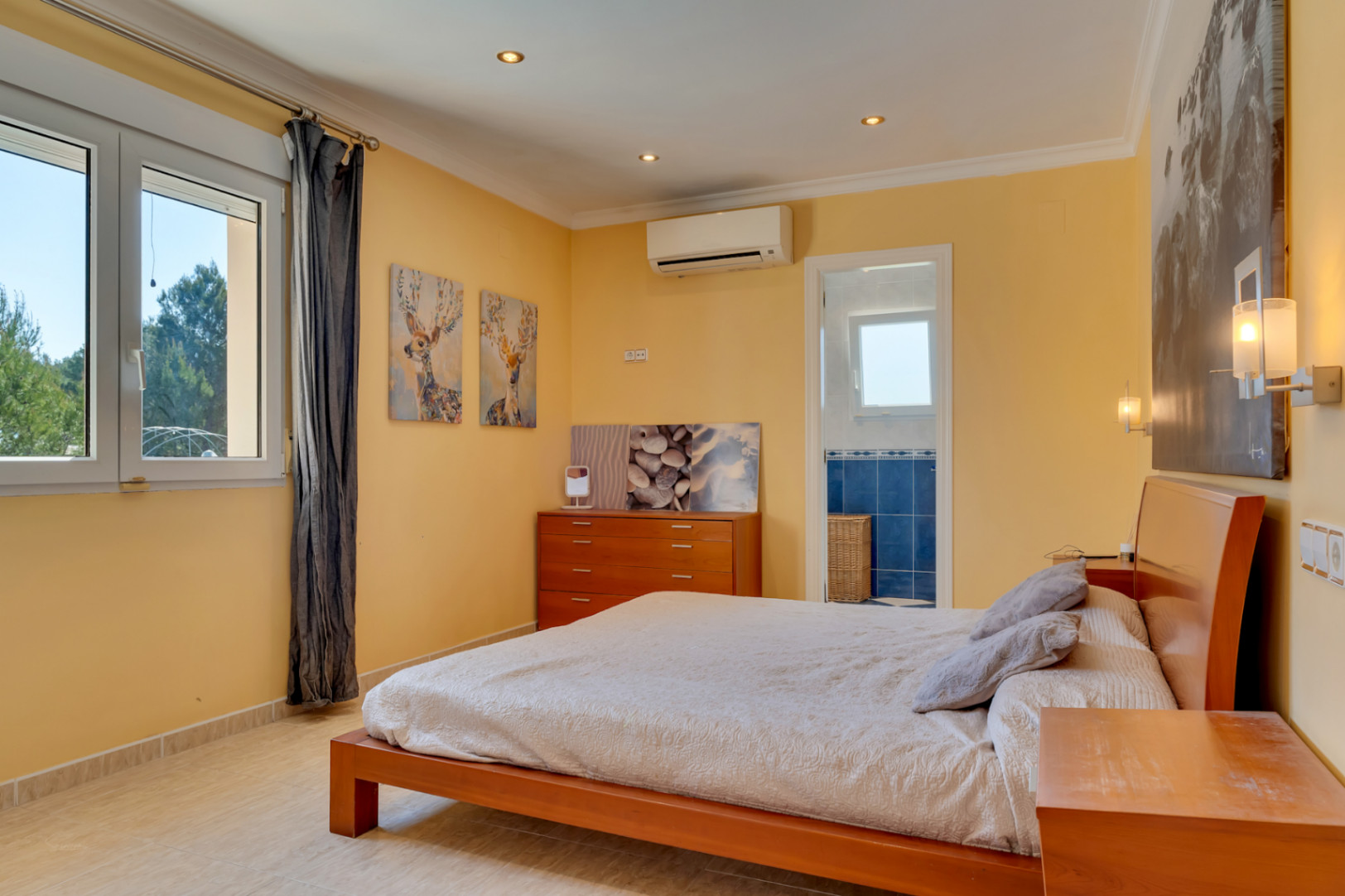 Dormitorio principal con baño en suite, aire acondicionado y ventanal de PVC. Cuenta con suelos cerámicos, mobiliario de madera y vistas al entorno natural.