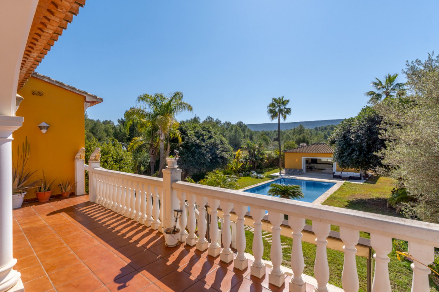 Terraza superior con balaustrada blanca y suelos de terracota, ofreciendo vistas despejadas a la piscina de 15x6m, el jardín mediterráneo y el entorno forestal.