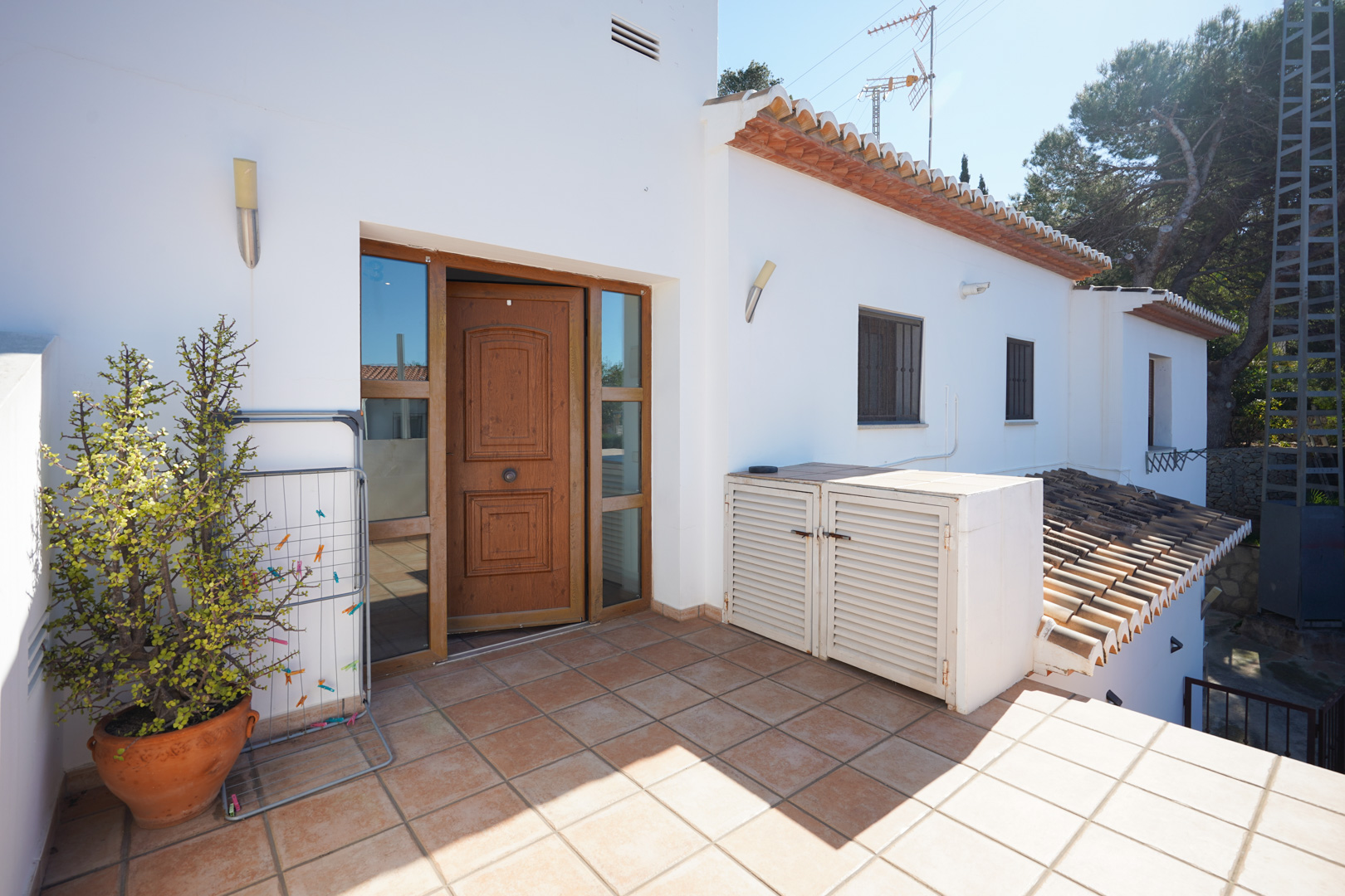 Acceso independiente a la vivienda superior con puerta de madera tallada, suelos de gres rústico y terraza abierta con armarios de almacenamiento exterior.