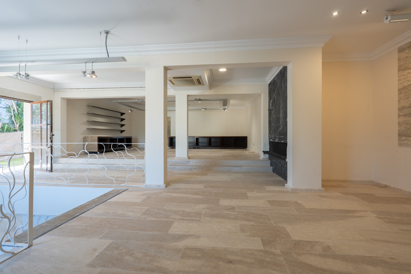 Amplio espacio diáfano con suelos de piedra natural, niveles escalonados y una pared revestida en mármol negro. Incluye iluminación técnica y barandilla artesanal.