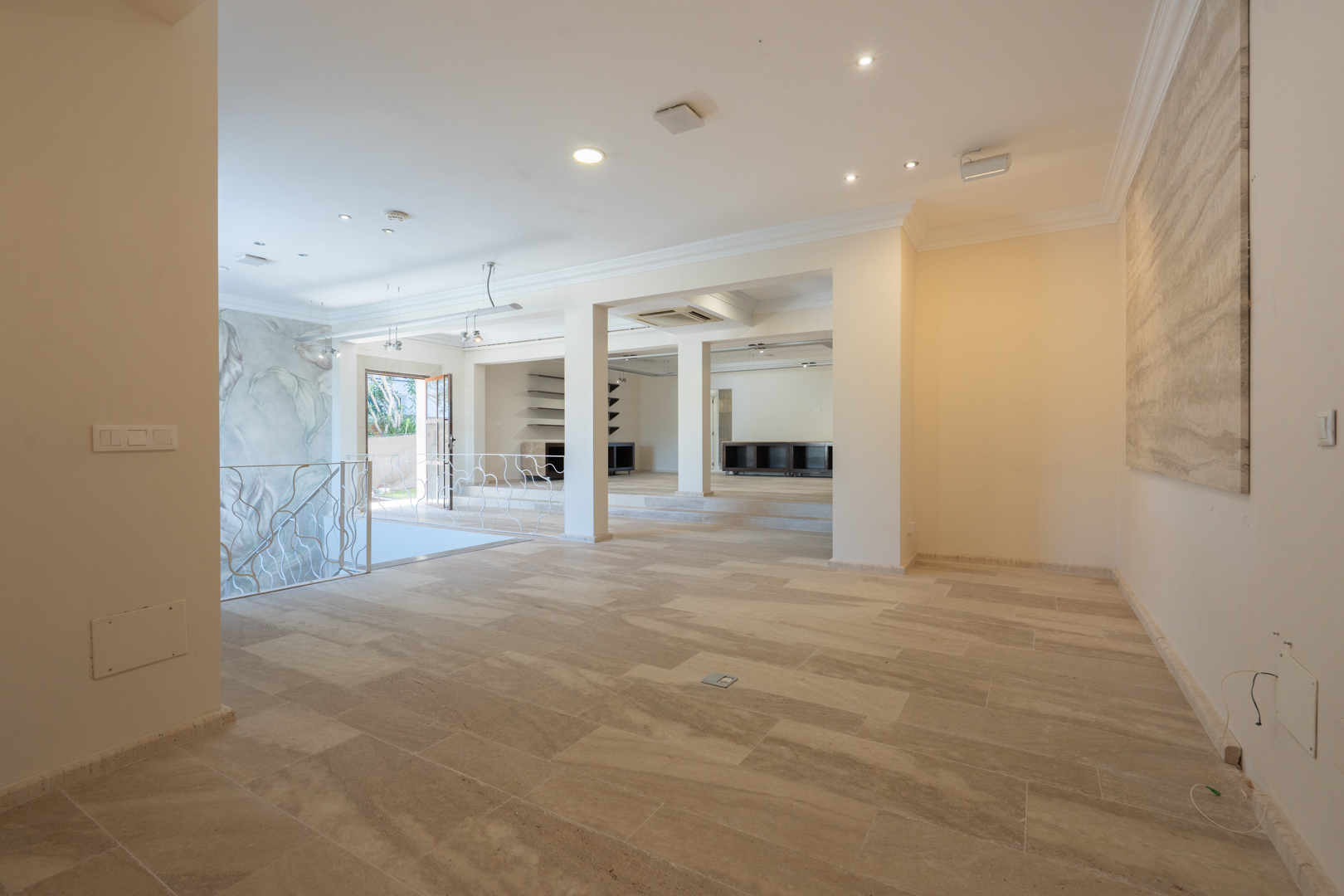 Amplio espacio diáfano en la primera planta con suelos de piedra natural, iluminación empotrada y una elegante barandilla de hierro forjado blanco.