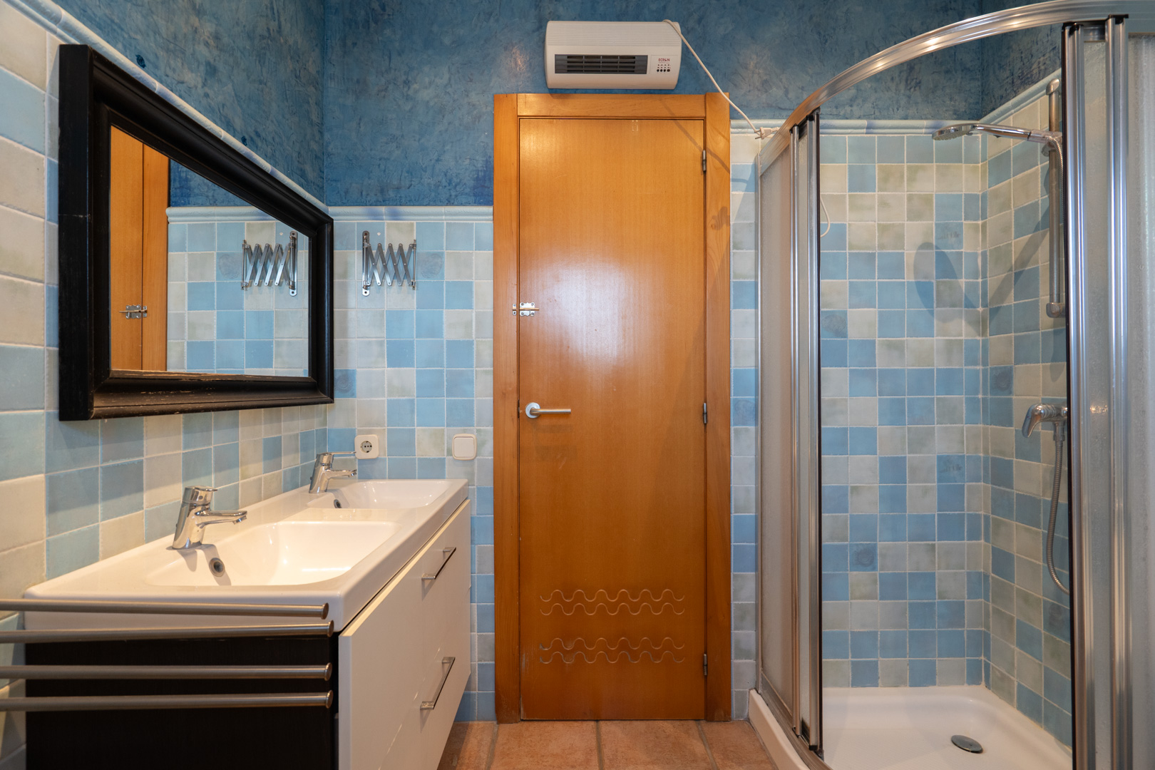 Baño funcional con lavabo doble, ducha de esquina con mampara curva y paredes decoradas con azulejos en degradado azul y pintura texturizada.