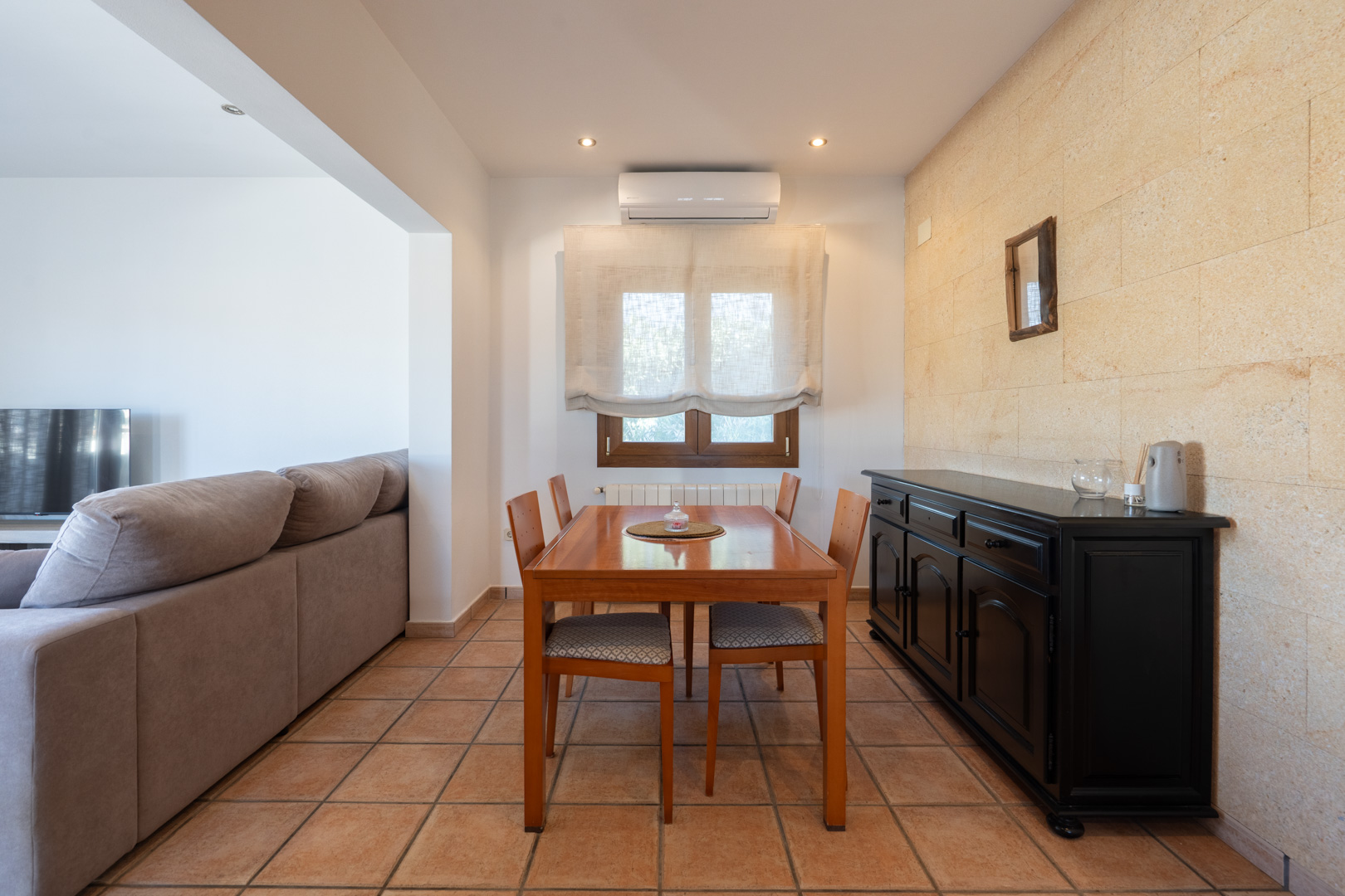 Comedor con pared de piedra natural, suelos de gres rústico, mesa de madera para cuatro comensales y aparador negro. Incluye aire acondicionado y calefacción.