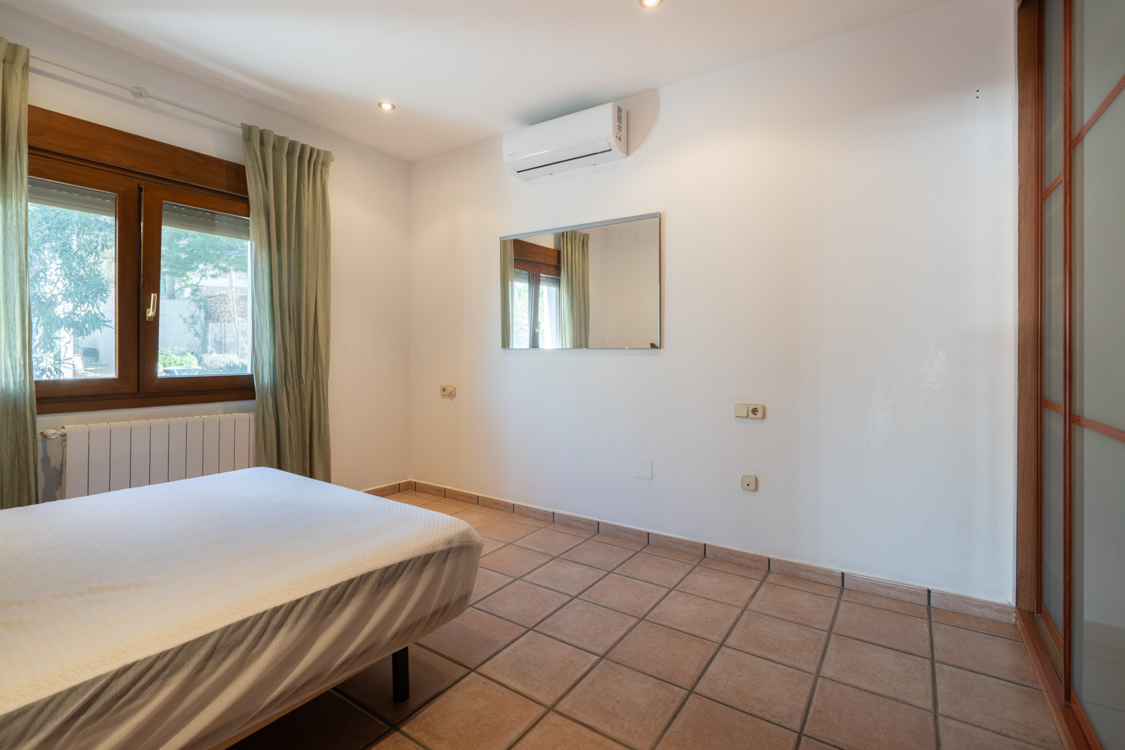 Dormitorio con suelos de gres, aire acondicionado split, ventana de madera y armario empotrado con puertas correderas translúcidas.