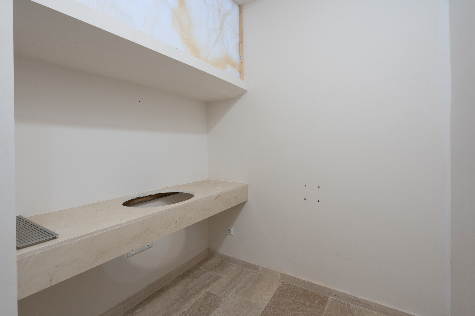 Encimera volada de piedra natural con hueco para lavabo, situada bajo una hornacina decorativa con panel de mármol retroiluminado y suelos de gres coordinados.
