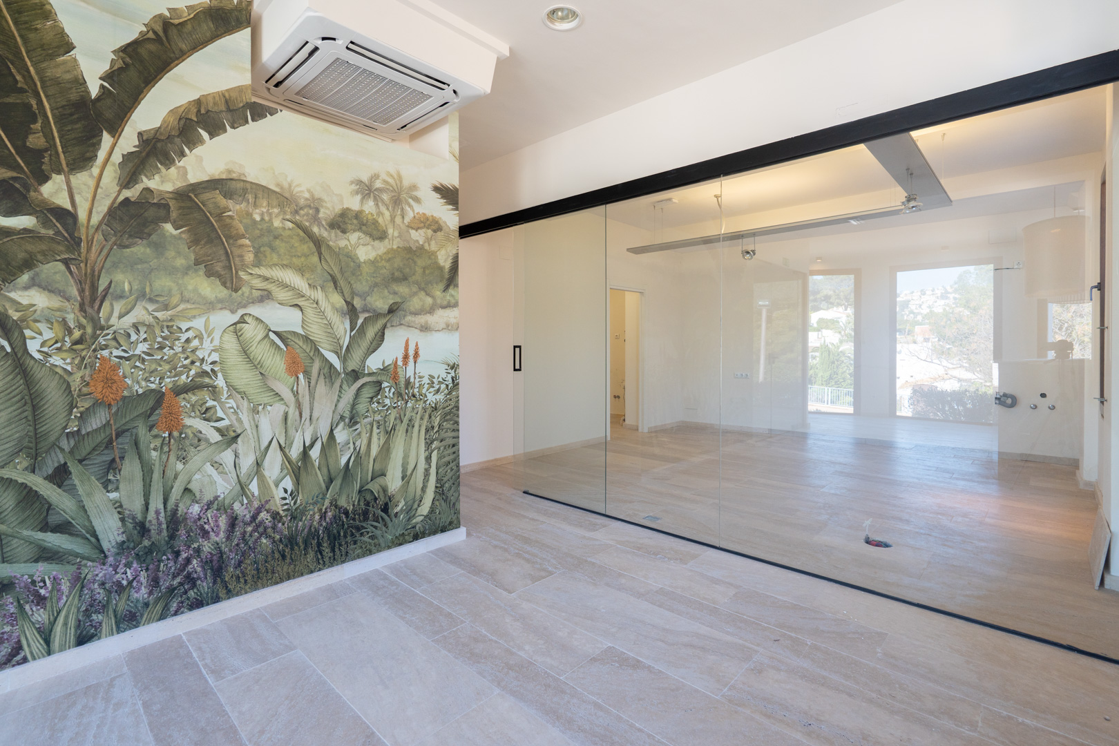 Espacio comercial diáfano con suelos cerámicos claros, mural de temática tropical y una gran partición de cristal con marcos negros que aporta luminosidad y amplitud.
