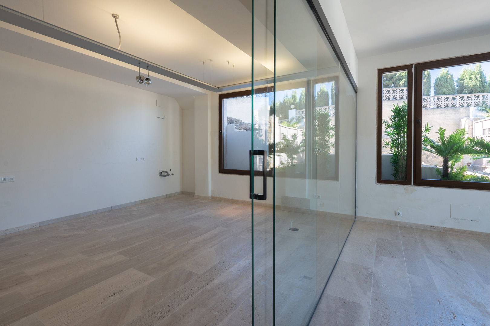Espacio comercial diáfano con suelos de piedra natural, mampara divisoria de cristal y ventanales que aportan luz natural y vistas al exterior.