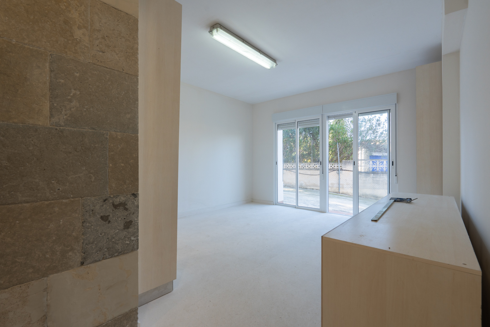 Espacio versátil en planta baja con pared de piedra natural, iluminación funcional y acceso directo al exterior mediante puertas correderas acristaladas.