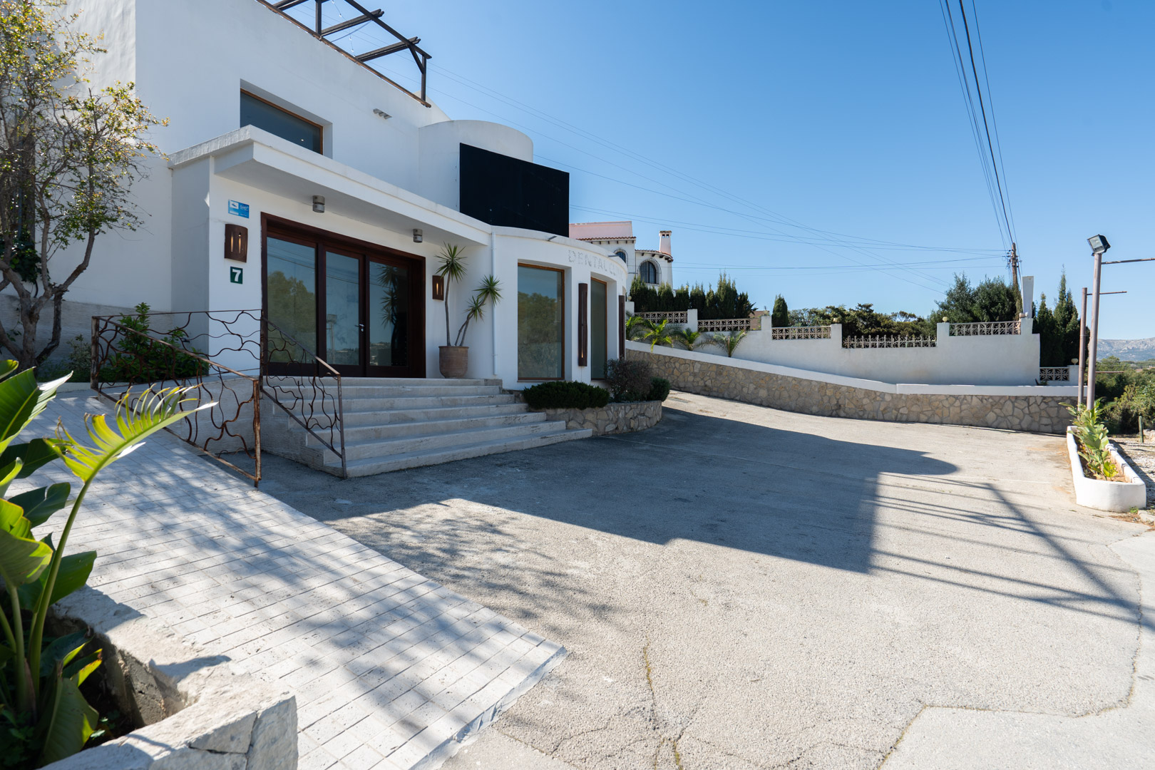 Fachada exterior con entrada principal acristalada, amplios escalones de piedra, rampa de acceso y zona de aparcamiento pavimentada bajo un cielo despejado.