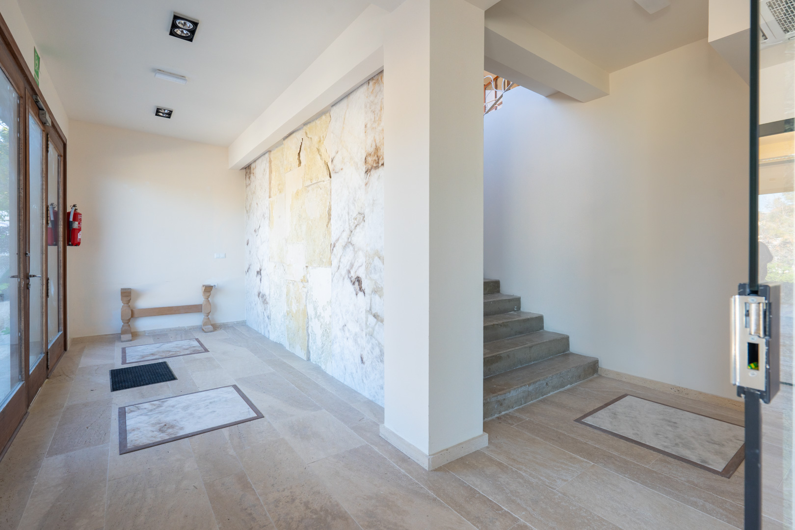 Hall de entrada con pared decorativa de piedra natural, suelos cerámicos con incrustaciones de mármol y acceso a la planta superior mediante escalera.