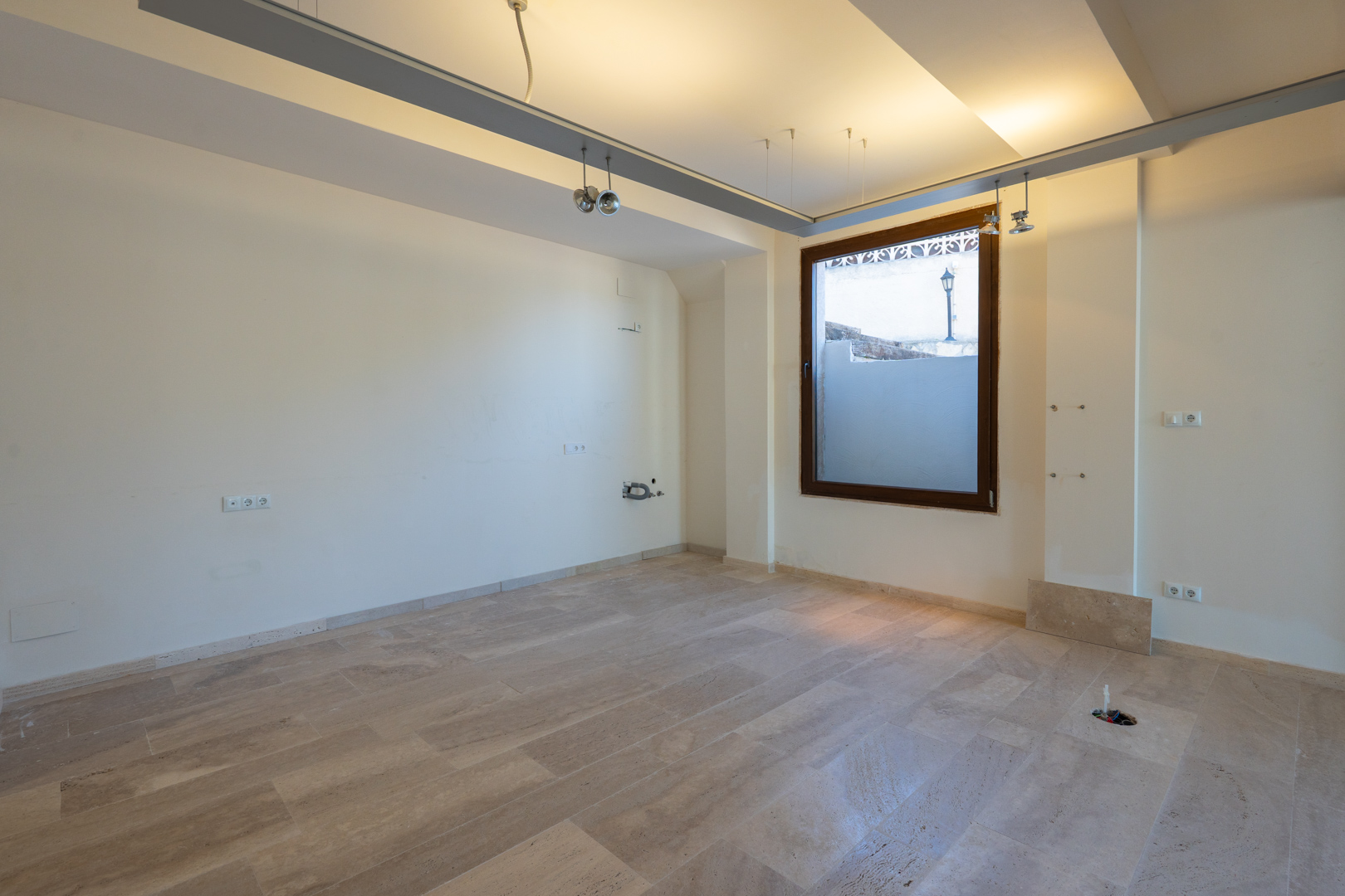 Sala diáfana con suelos de piedra natural, iluminación técnica mediante rieles y preinstalación de suministros, ideal para adaptar como oficina o local comercial.