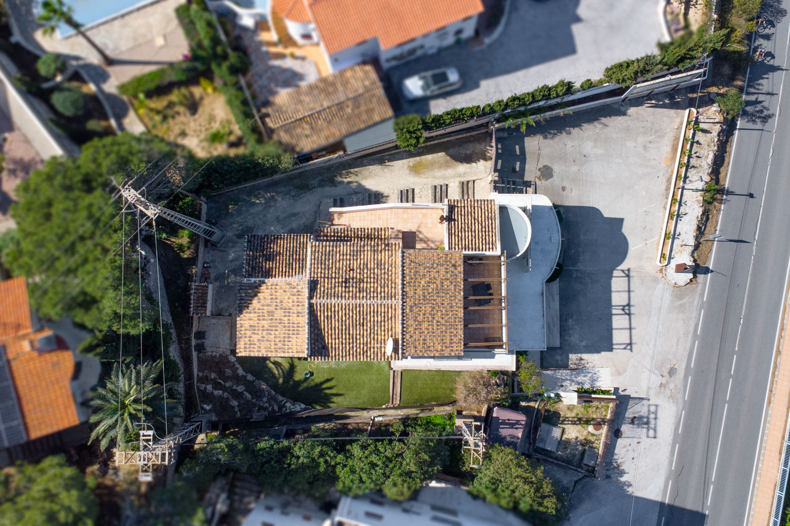 Vista aérea cenital que muestra la distribución de la propiedad, sus tejados de teja cerámica, las terrazas exteriores y la amplia zona de aparcamiento junto a la carretera principal.
