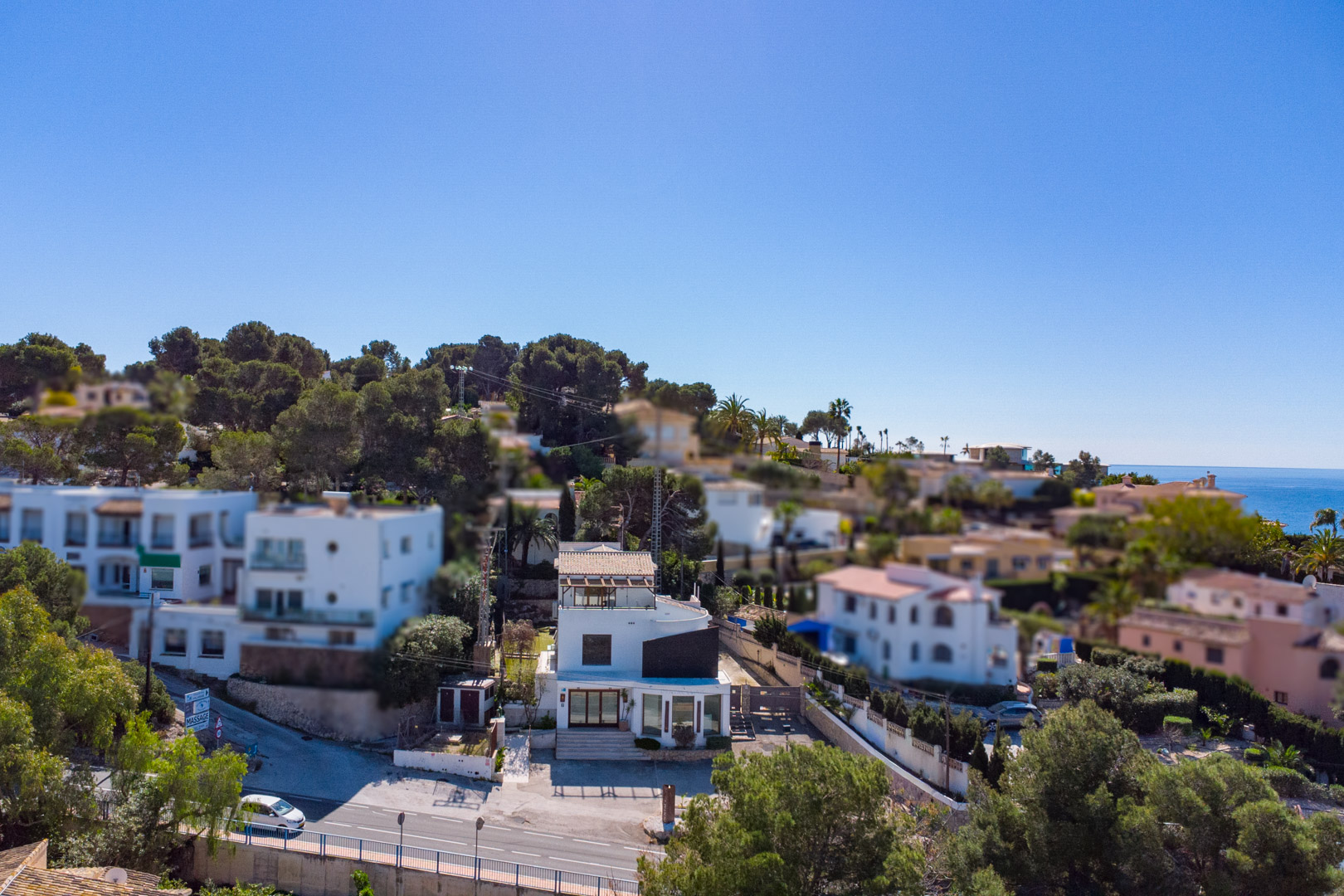 Vista aérea de la propiedad de tres plantas junto a la carretera, destacando su fachada blanca, amplios ventanales comerciales y terraza superior con pérgola.