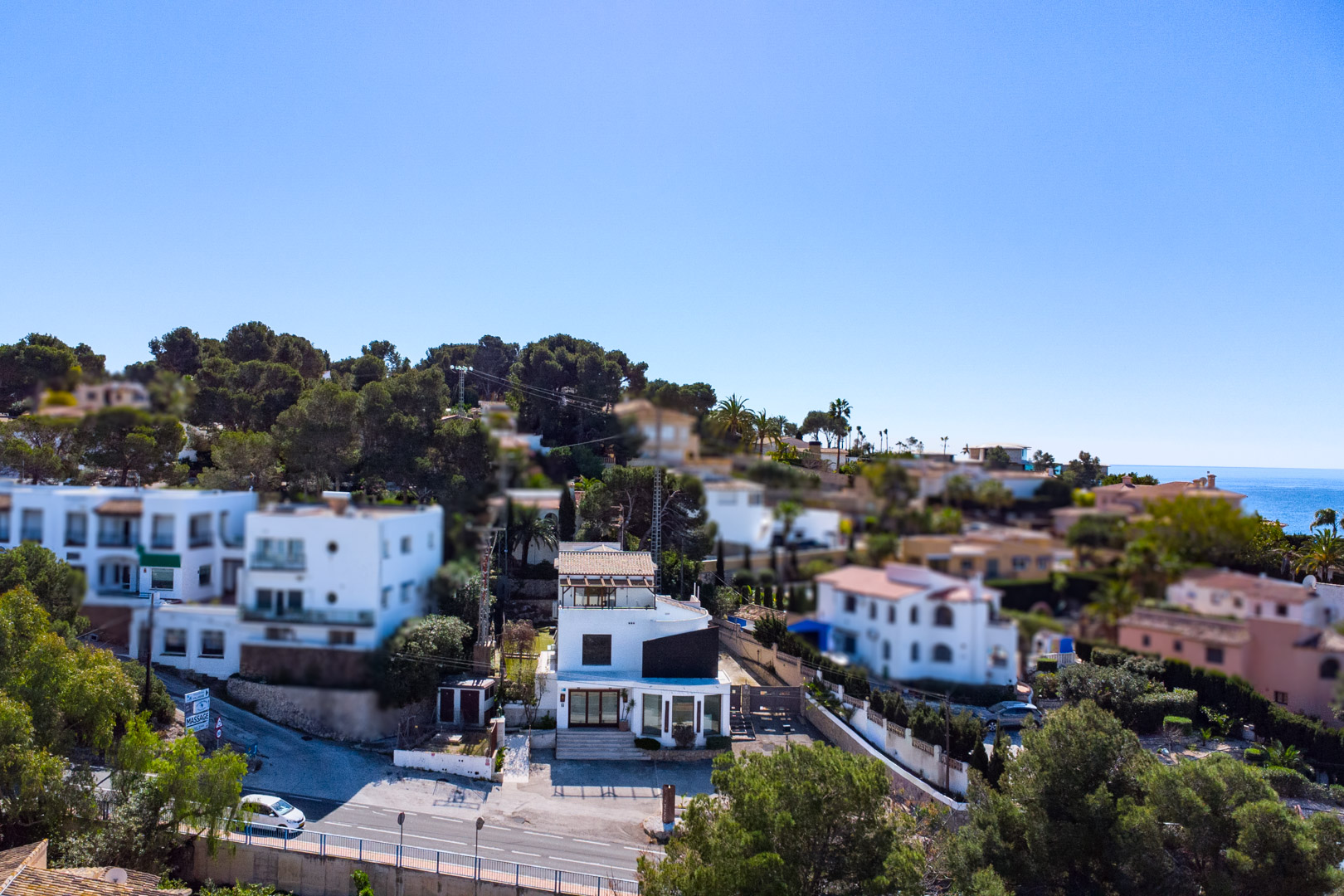 Vista aérea de la propiedad junto a la carretera Moraira-Calpe, con fachada blanca, grandes ventanales comerciales y vistas al mar Mediterráneo al fondo.