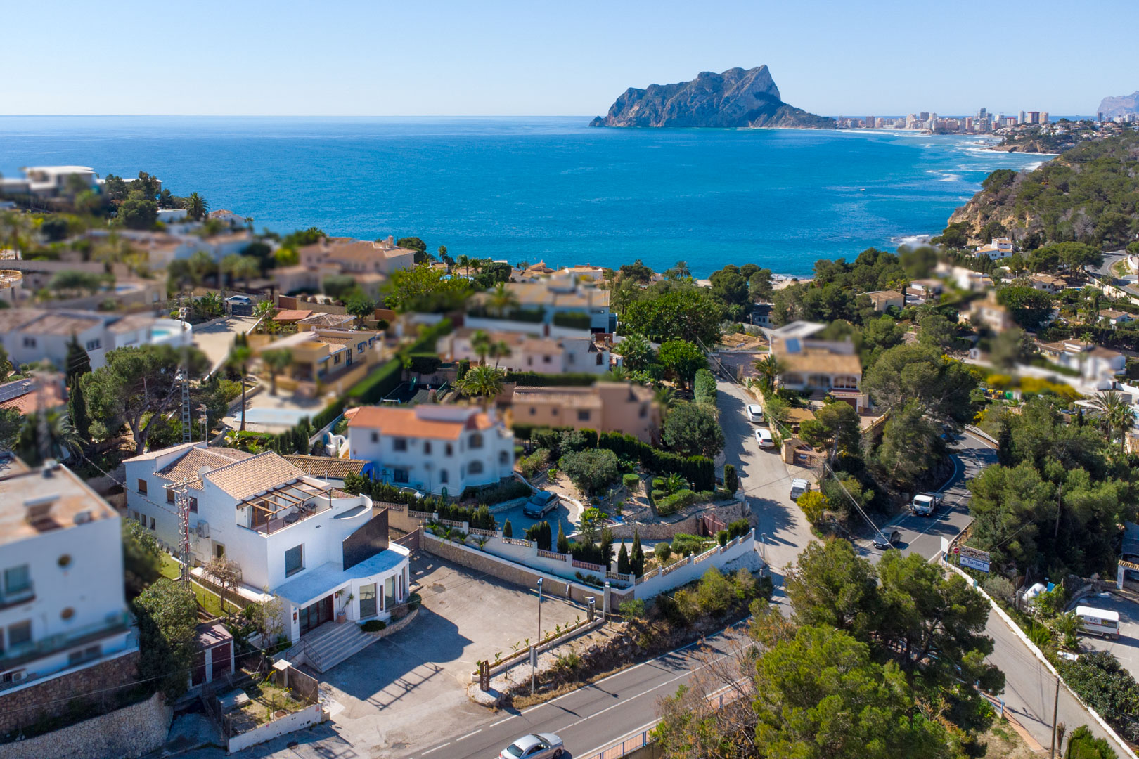 Vista aérea que muestra la ubicación estratégica del edificio junto a la carretera, con amplio aparcamiento frontal y vistas panorámicas al mar y al Peñón de Ifach.
