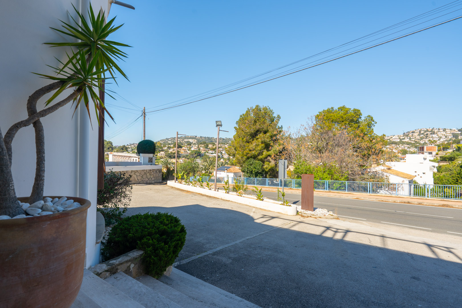Zona de aparcamiento exterior y acceso principal con gran visibilidad desde la carretera, rodeada de vegetación mediterránea y vistas despejadas a las colinas.