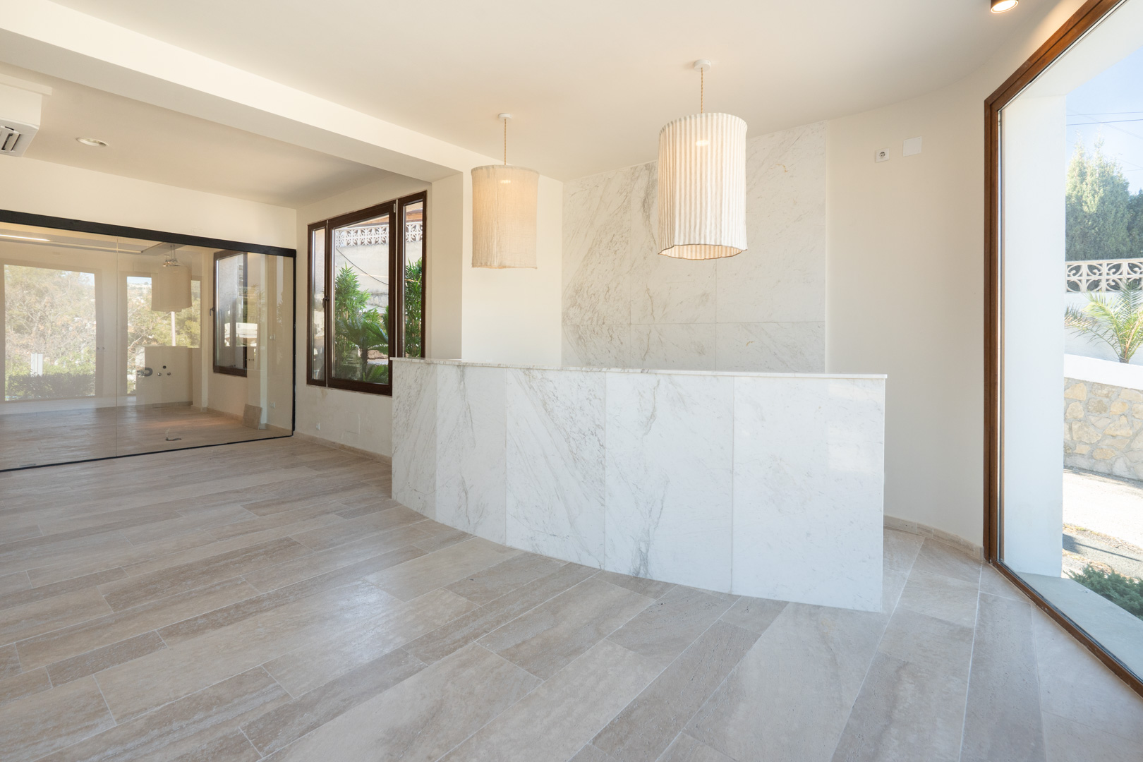 Zona de recepción con mostrador de mármol blanco, suelos de gres porcelánico y lámparas colgantes de tela en un espacio comercial de diseño diáfano.