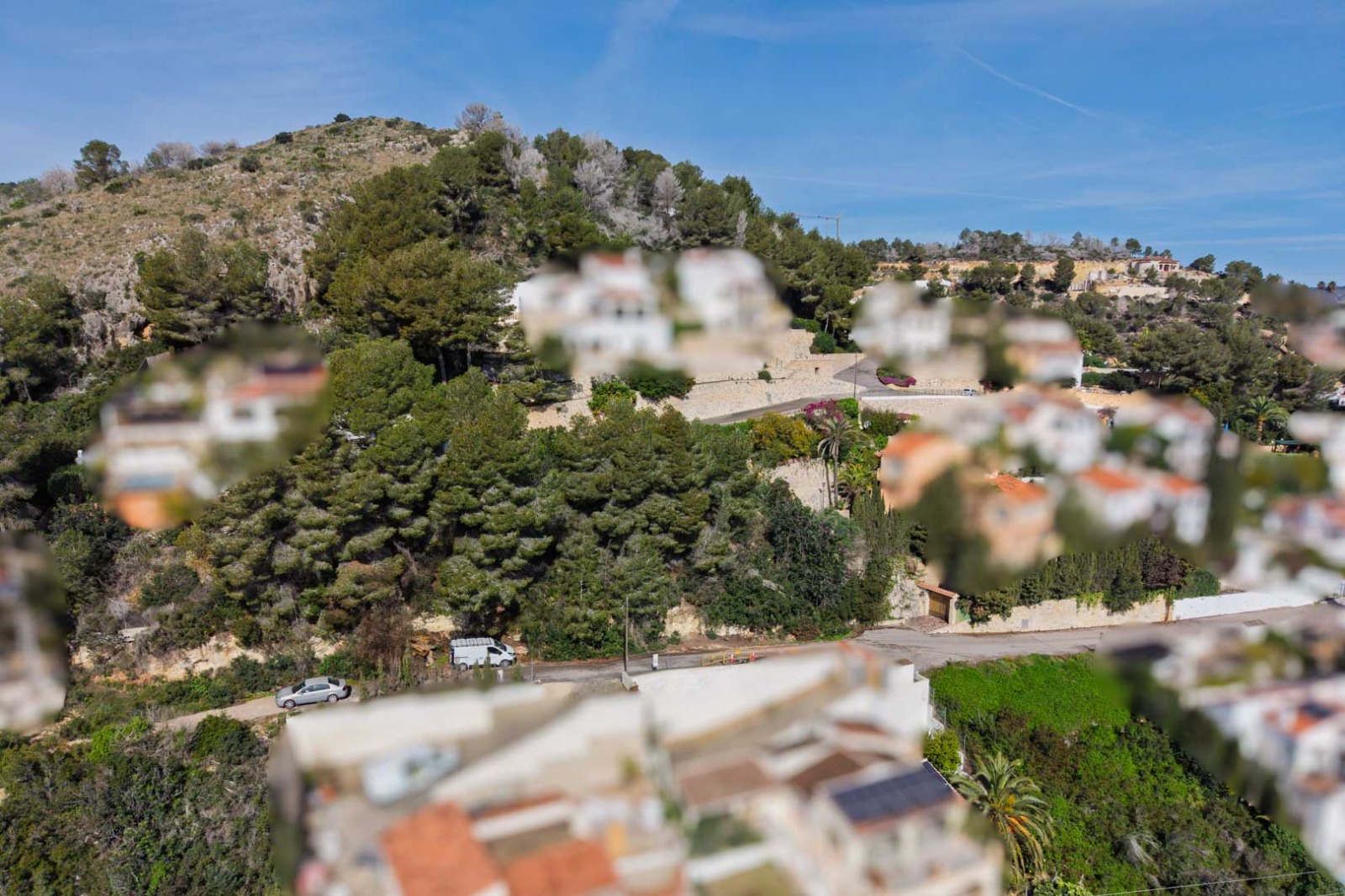 Vista aérea de la ladera boscosa en Sol de Este, mostrando la integración de villas mediterráneas entre pinos y calles asfaltadas con muros de piedra.
