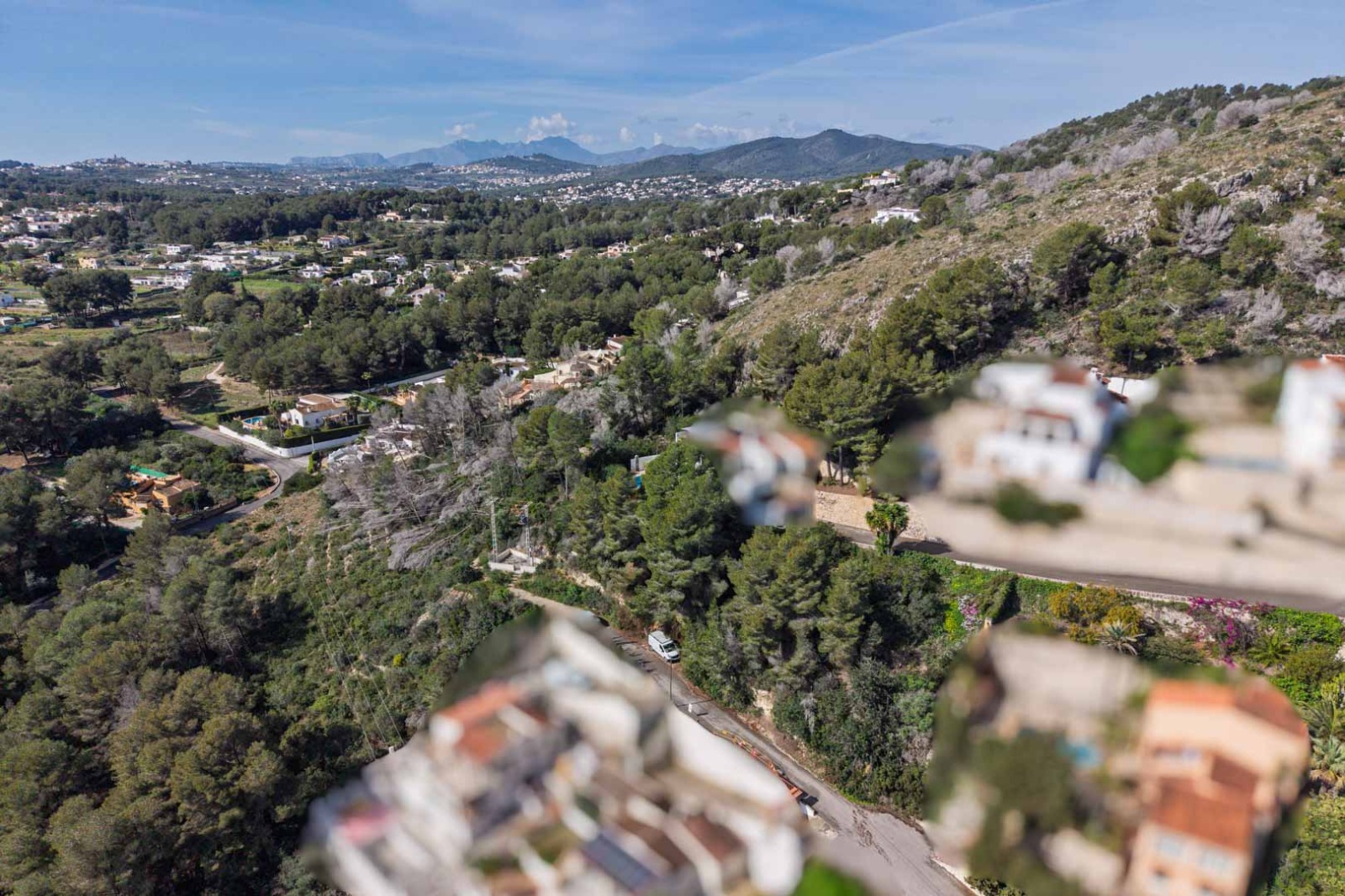 Vista aérea de la urbanización Sol de Este, mostrando la densa vegetación de pinos, las colinas circundantes y el relieve montañoso bajo un cielo despejado.