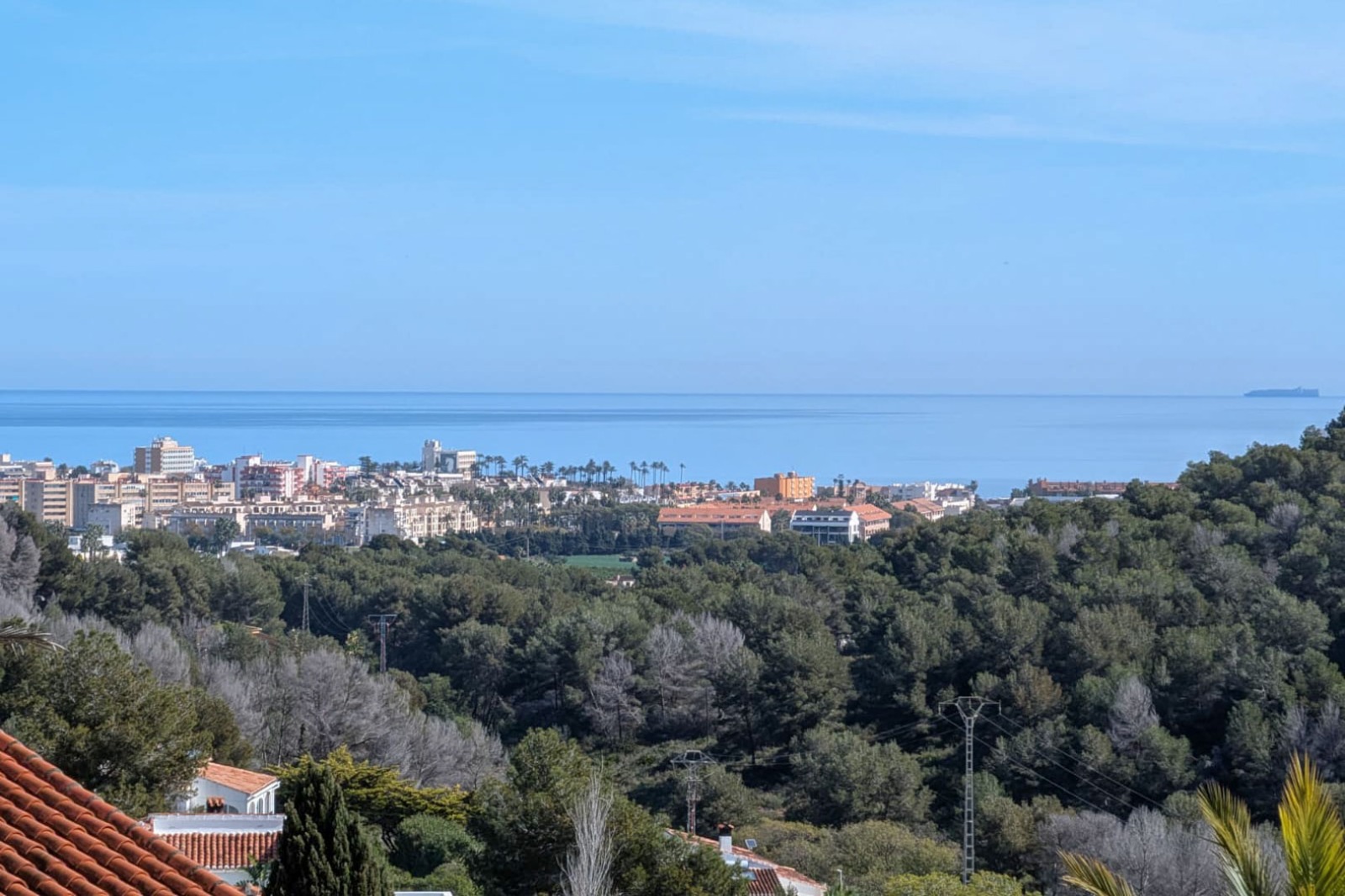 Vistas panorámicas desde la parcela hacia el mar Mediterráneo, con el núcleo urbano de Jávea y colinas boscosas en primer plano bajo un cielo despejado.