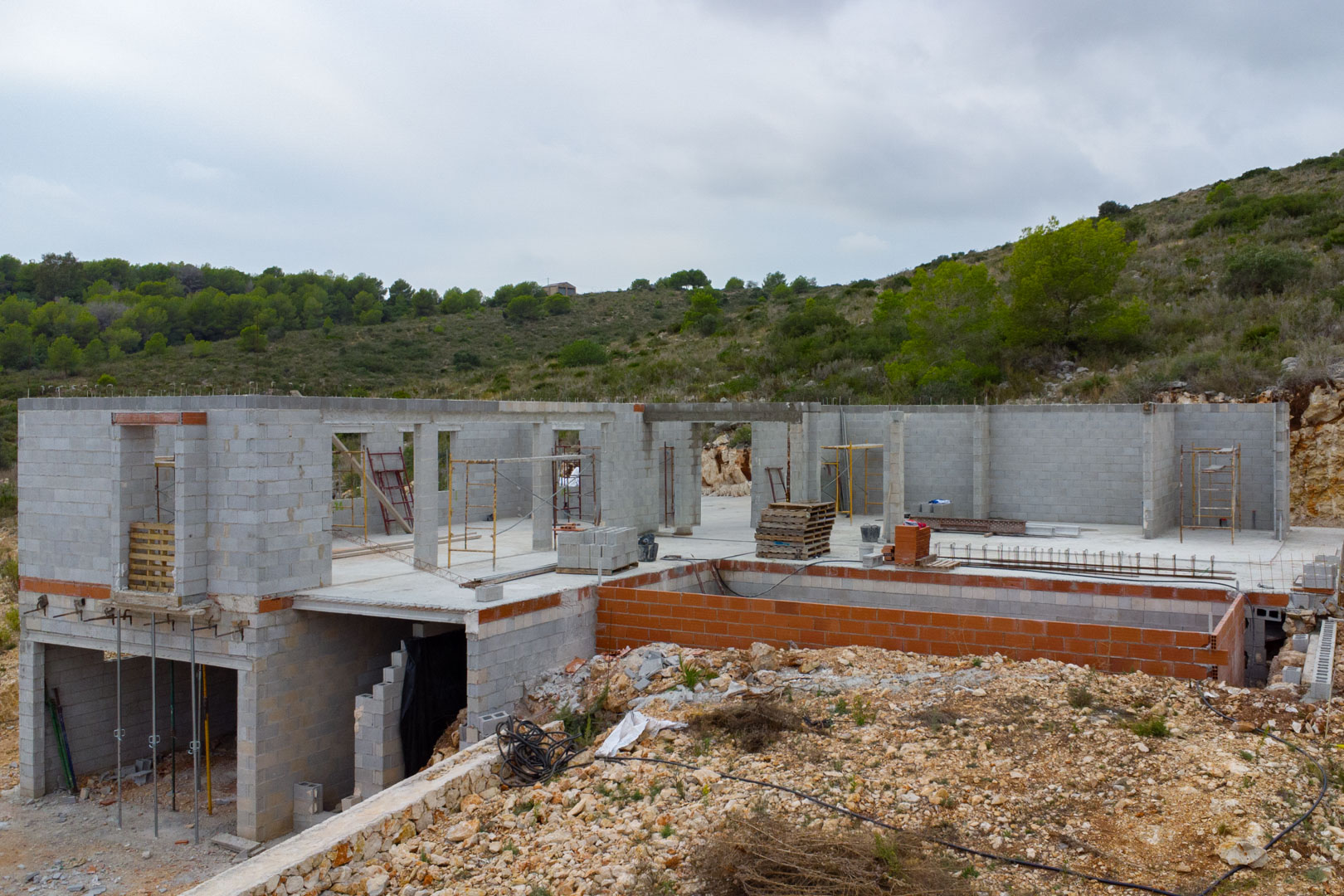 Villa moderna en construcción en Pedreguer con muros de bloques de hormigón, estructura para piscina y una ubicación elevada con vistas a la montaña.