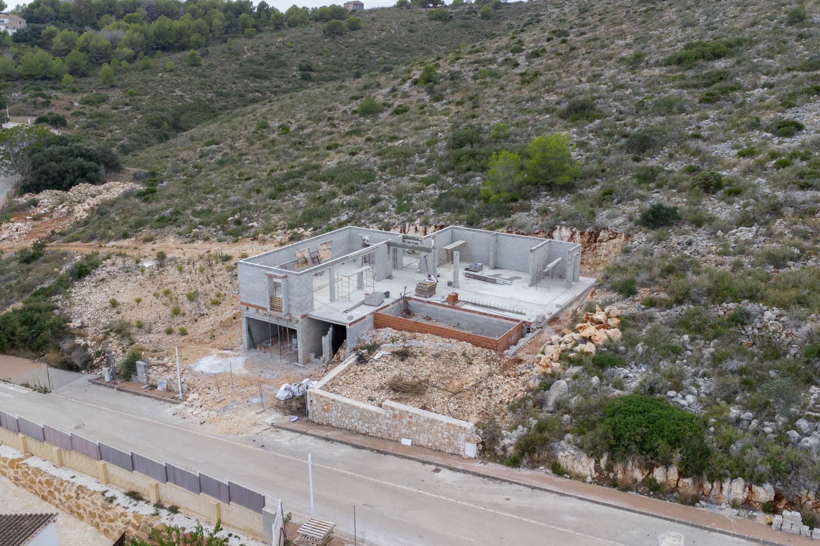 Vista aérea del progreso de construcción de la villa en Pedreguer, destacando la estructura de bloques de hormigón integrada en la ladera natural.