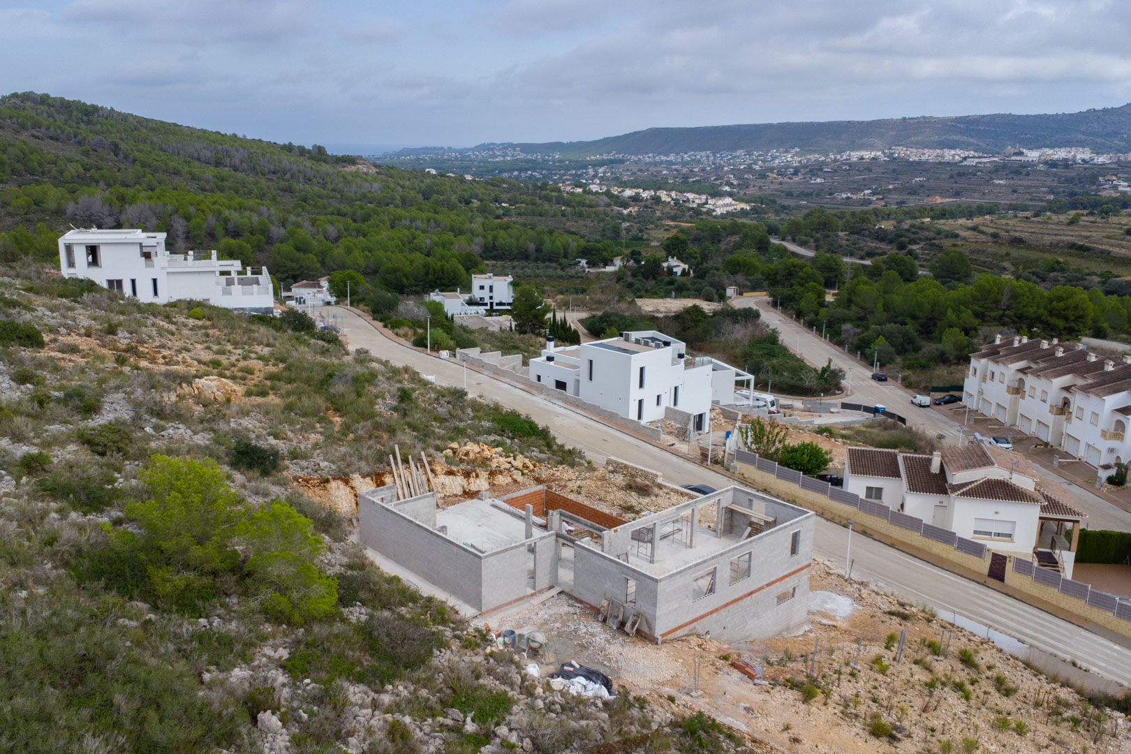 Vista elevada de la villa en construcción en Pedreguer, mostrando la estructura de hormigón sobre una ladera con vistas panorámicas al valle y montañas.