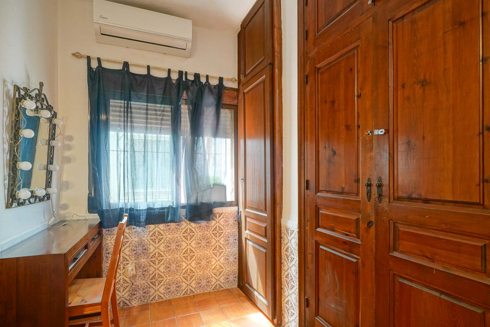 Rincón de tocador con escritorio de madera y espejo iluminado, junto a amplios armarios empotrados de madera oscura y paredes con zócalo de azulejo tradicional.