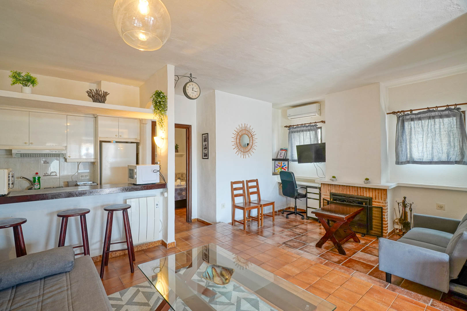 Salón comedor con chimenea de obra, suelos de gres rústico y cocina semiabierta con barra americana y taburetes de madera.