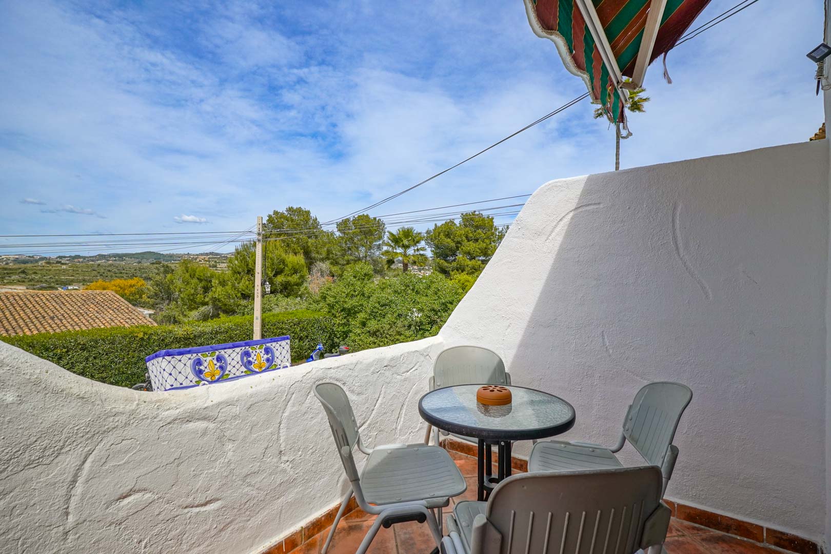 Terraza exterior con suelo de gres cerámico y mobiliario de exterior, ofreciendo vistas despejadas al valle y entorno arbolado de Moraira bajo un toldo retráctil.