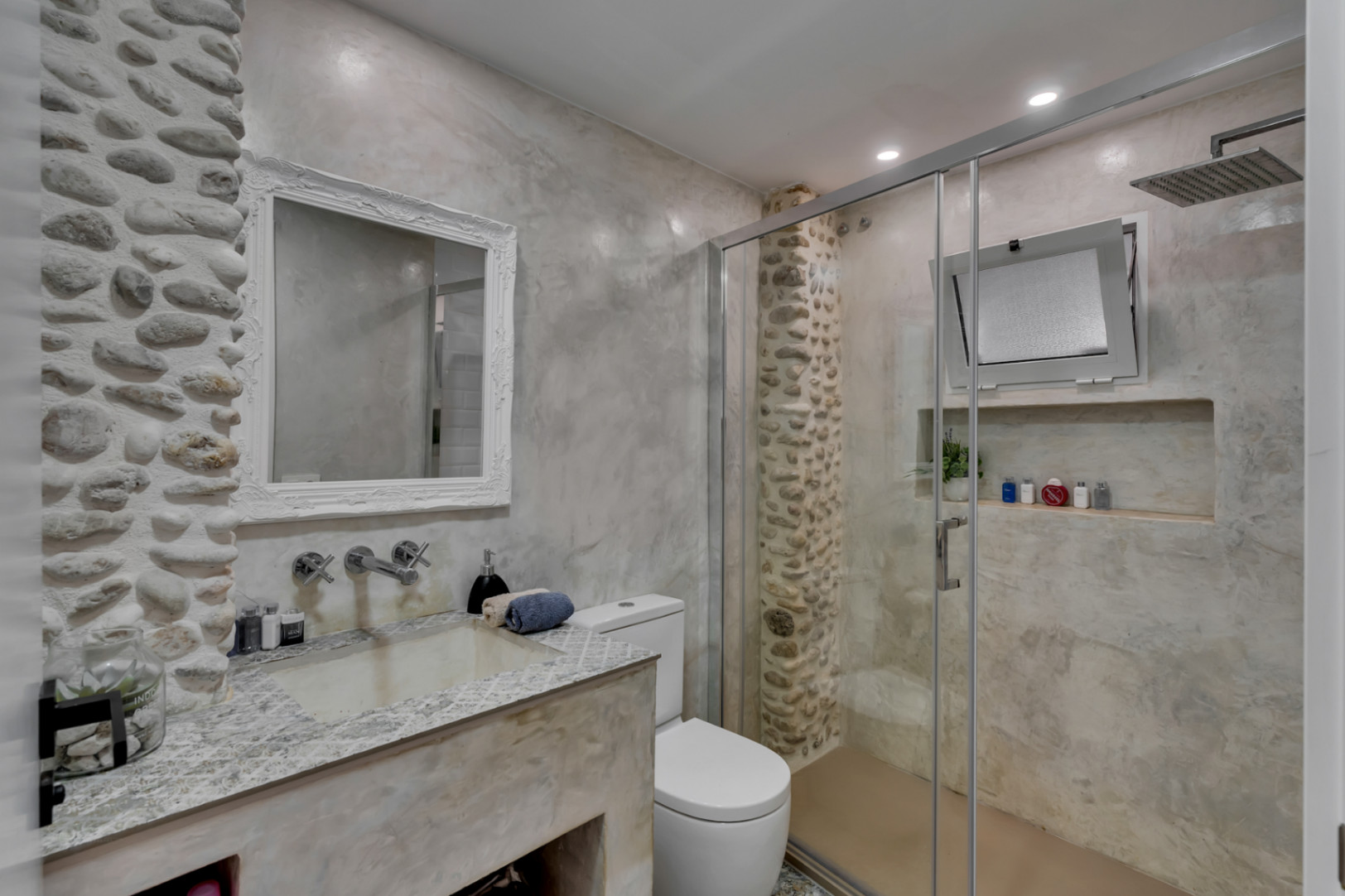 Detalle del baño con paredes de piedra y ducha con mampara de cristal.