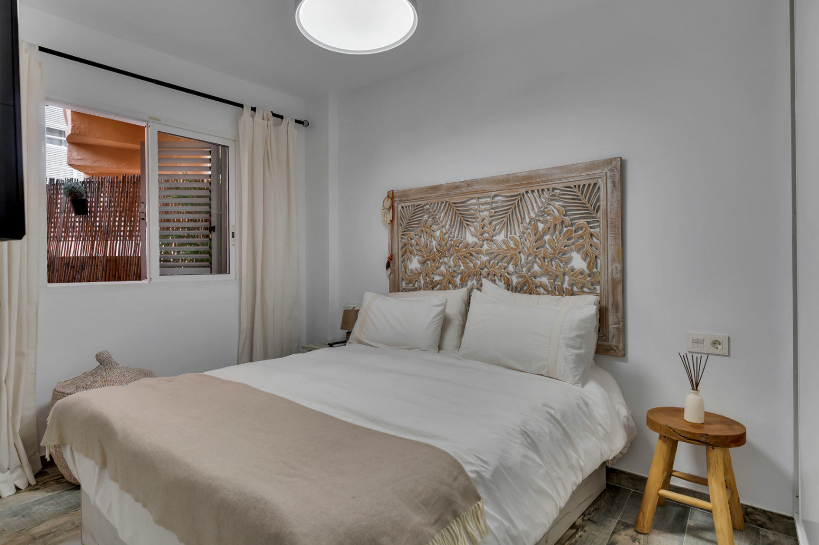 Dormitorio luminoso con cabecero de madera tallada y vistas a la terraza.