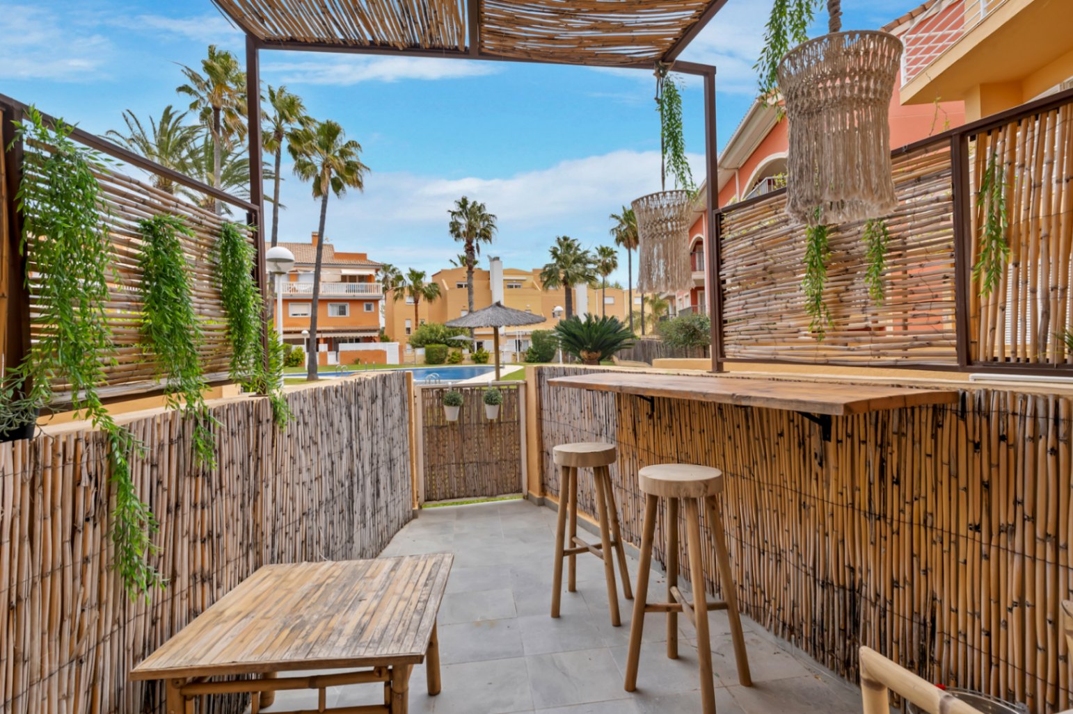 Terraza privada con barra de bambú y vistas a la piscina comunitaria y jardines.