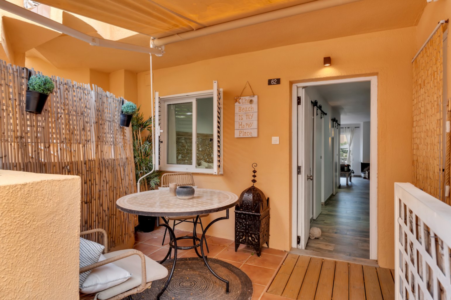 Terraza privada con suelo de baldosas, mesa redonda con sillas de mimbre y decoración de estilo bohemio.