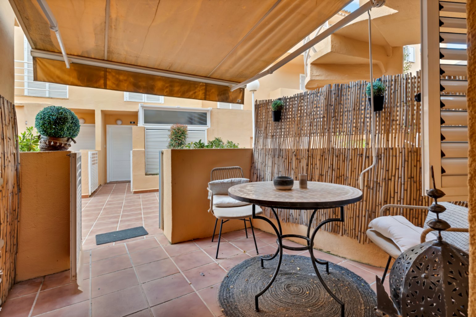 Terraza privada con toldo, suelo de baldosas rojizas y mobiliario de exterior con detalles bohemios.