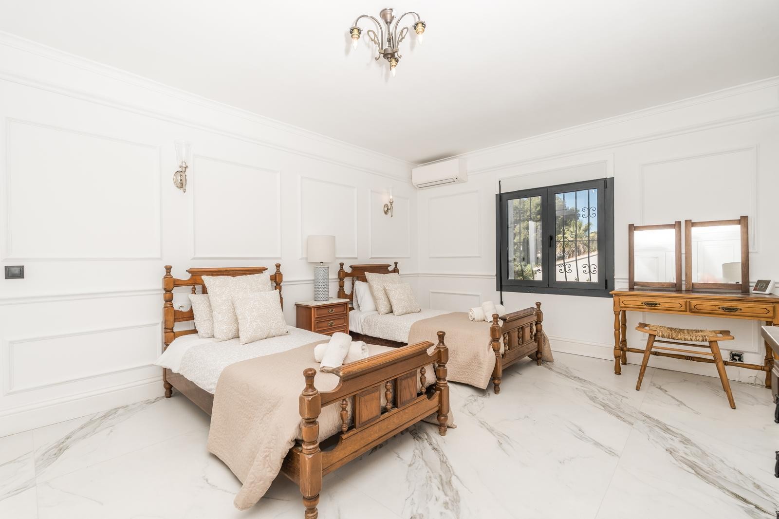 Dormitorio con dos camas individuales de madera tallada, suelos de mármol blanco y paredes decoradas con molduras elegantes y aire acondicionado.
