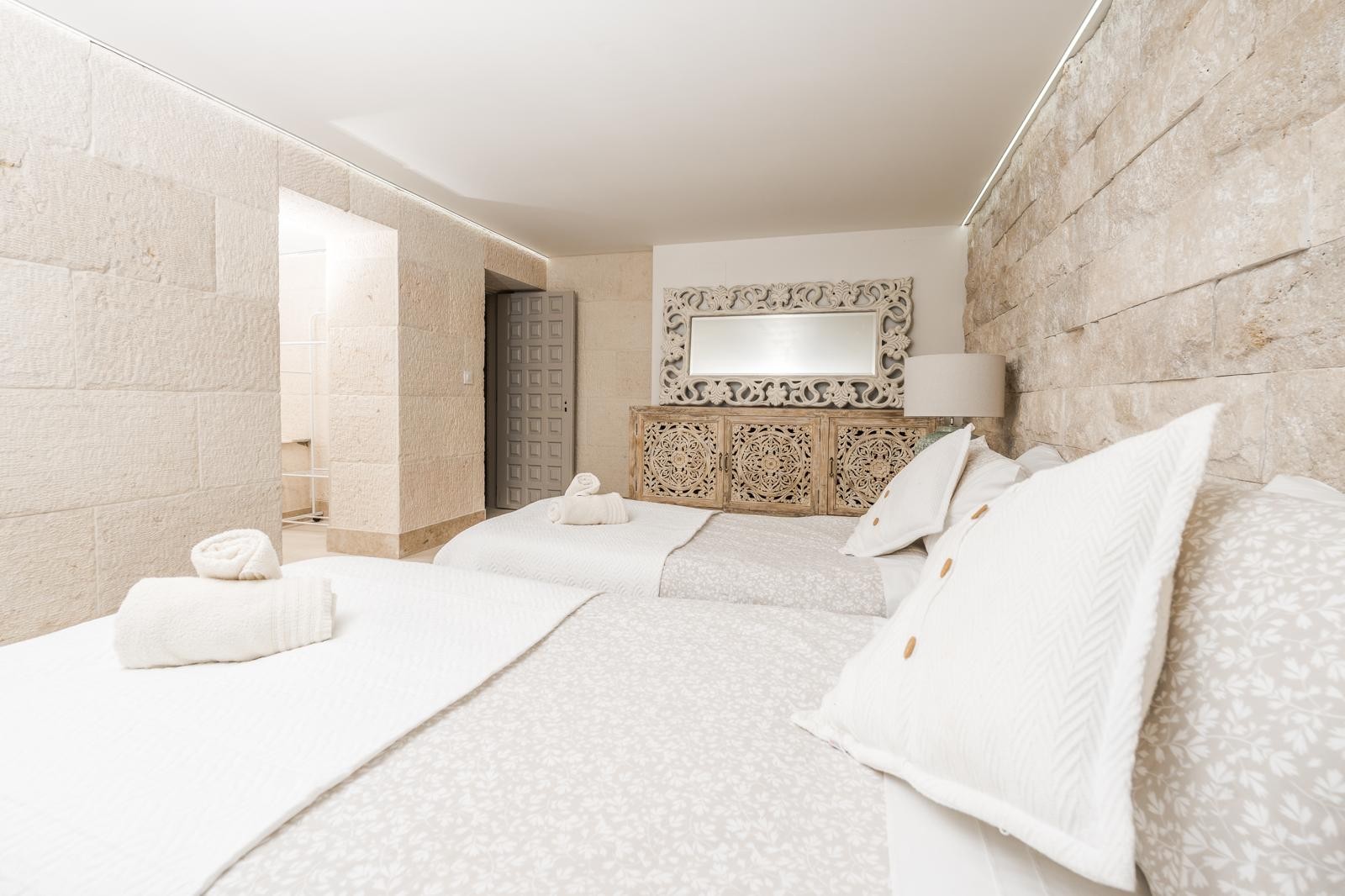 Dormitorio con paredes de piedra natural, mobiliario de madera tallada de estilo mediterráneo e iluminación LED indirecta integrada en el techo.
