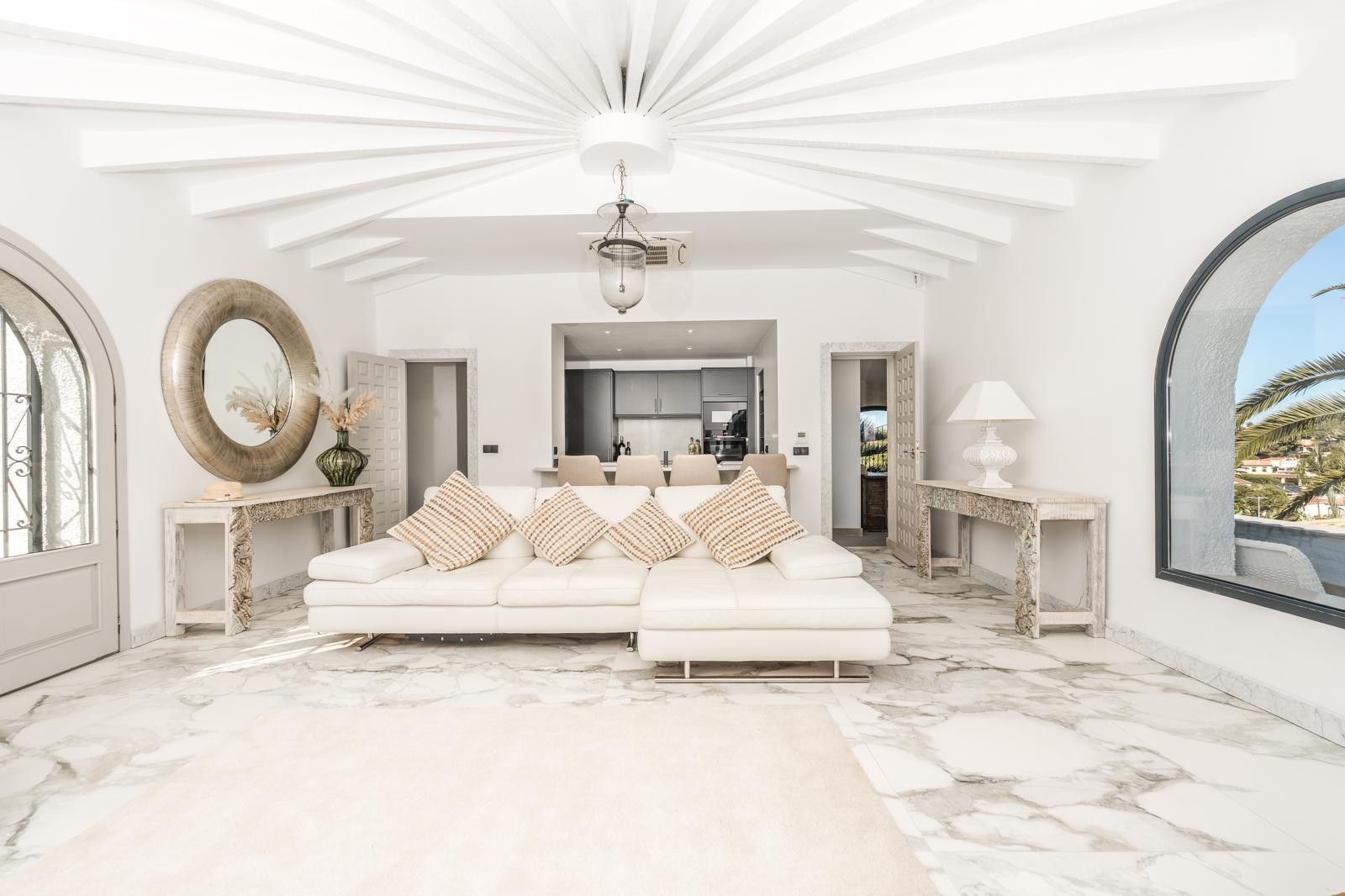 Salón de diseño circular con techo de vigas radiales, suelos de mármol y un gran ventanal de arco. La estancia conecta visualmente con la cocina y destaca por su luminosidad.