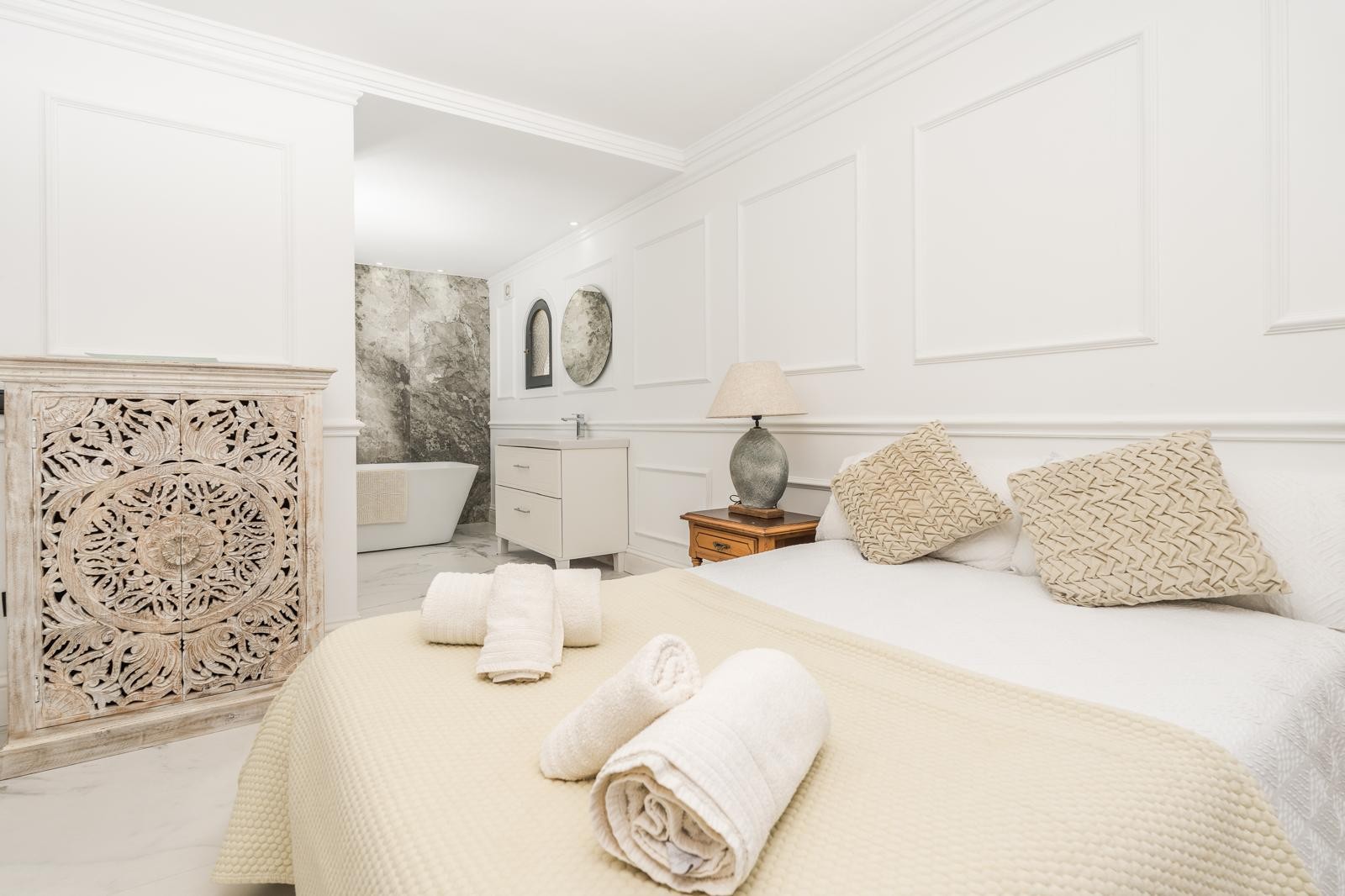 Suite principal con concepto abierto que integra el baño, destacando una bañera exenta ante una pared de mármol gris y paredes con molduras decorativas clásicas.