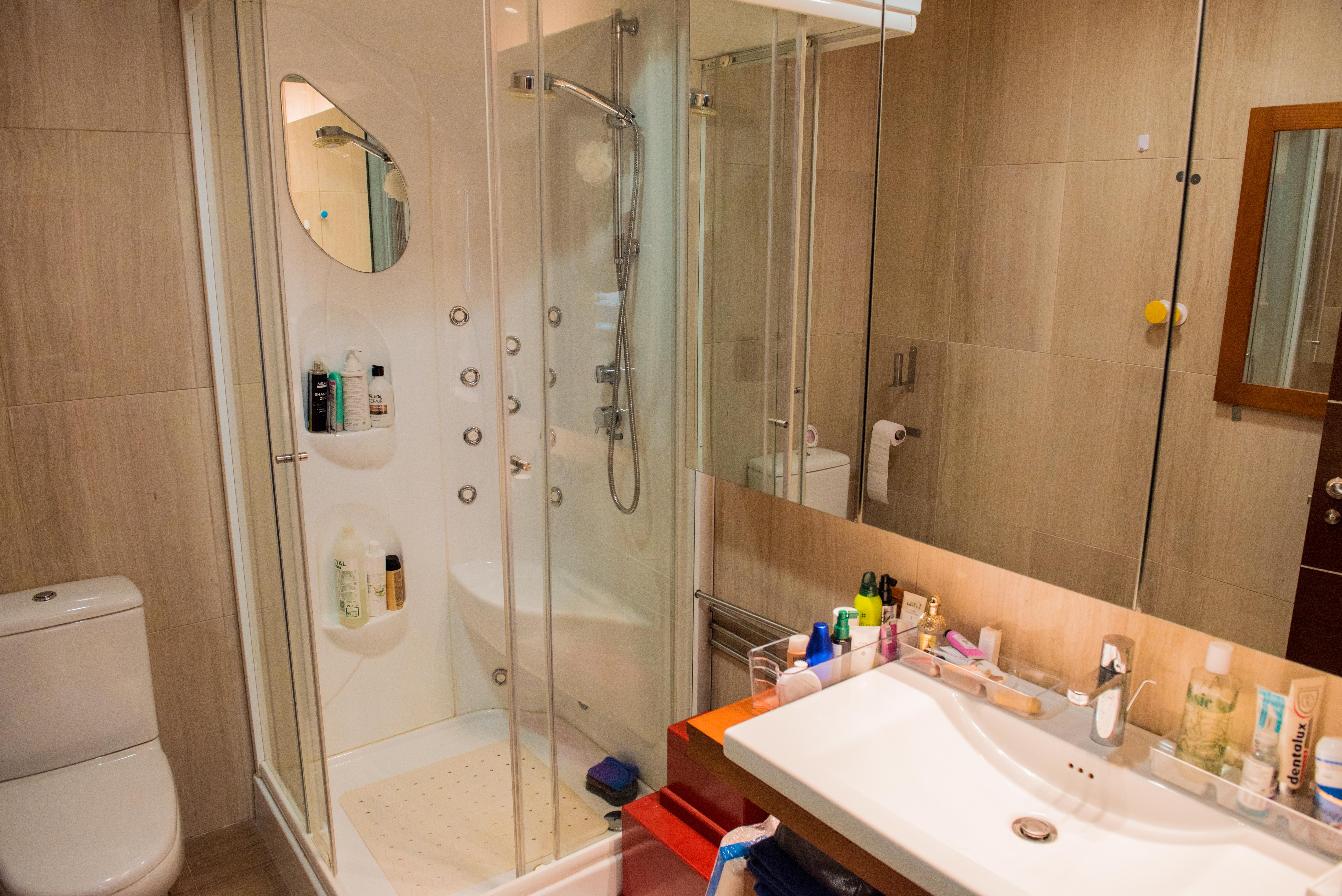 Baño moderno con cabina de ducha de hidromasaje, mampara de cristal, lavabo blanco de diseño y paredes revestidas en gres porcelánico de tonos neutros.