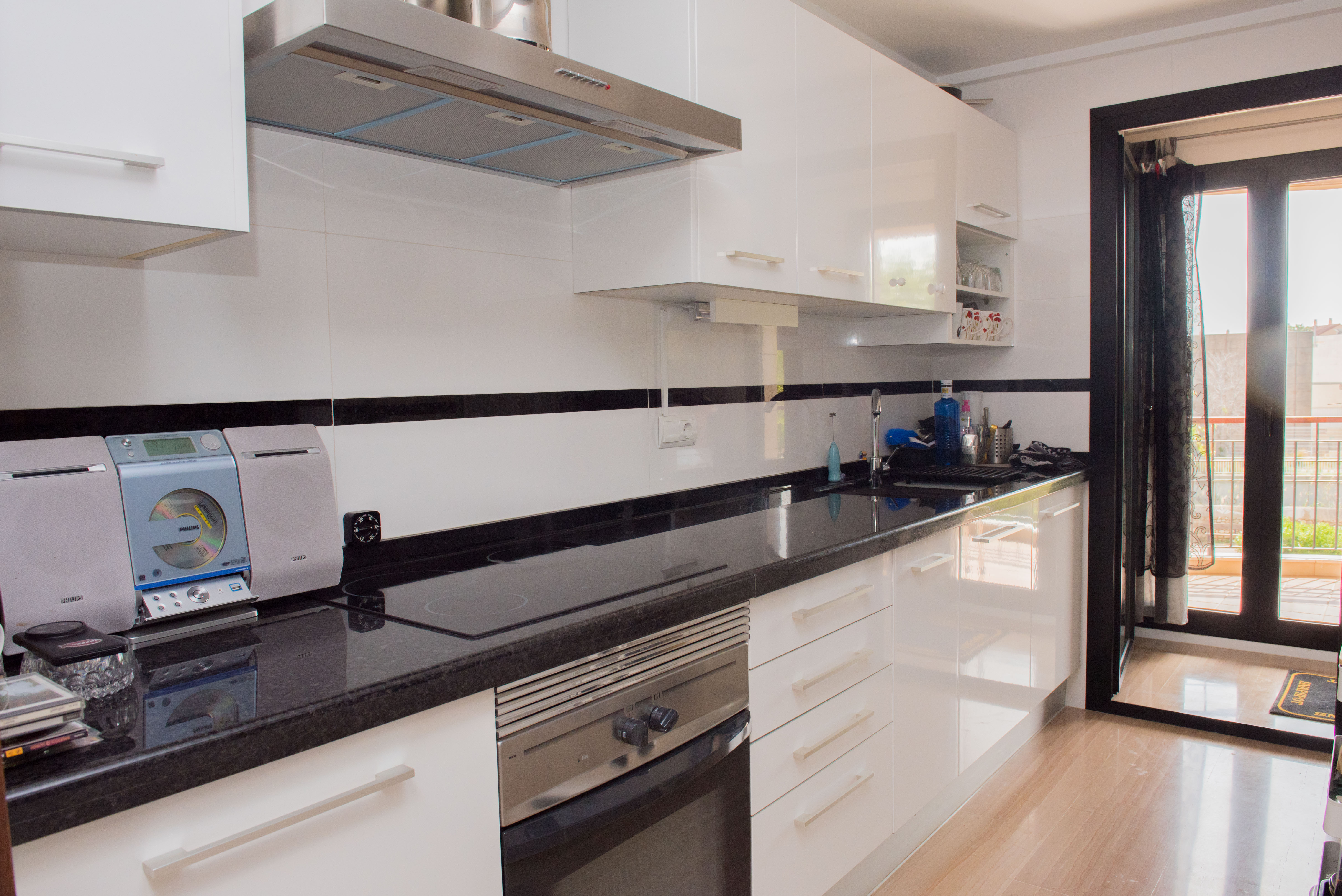 Cocina moderna con armarios blancos brillantes, encimera de granito oscuro, electrodomésticos integrados y acceso a un balcón. Cocina moderna con armarios blancos brillantes, encimera de granito oscuro, electrodomésticos integrados y acceso a un balcón.
