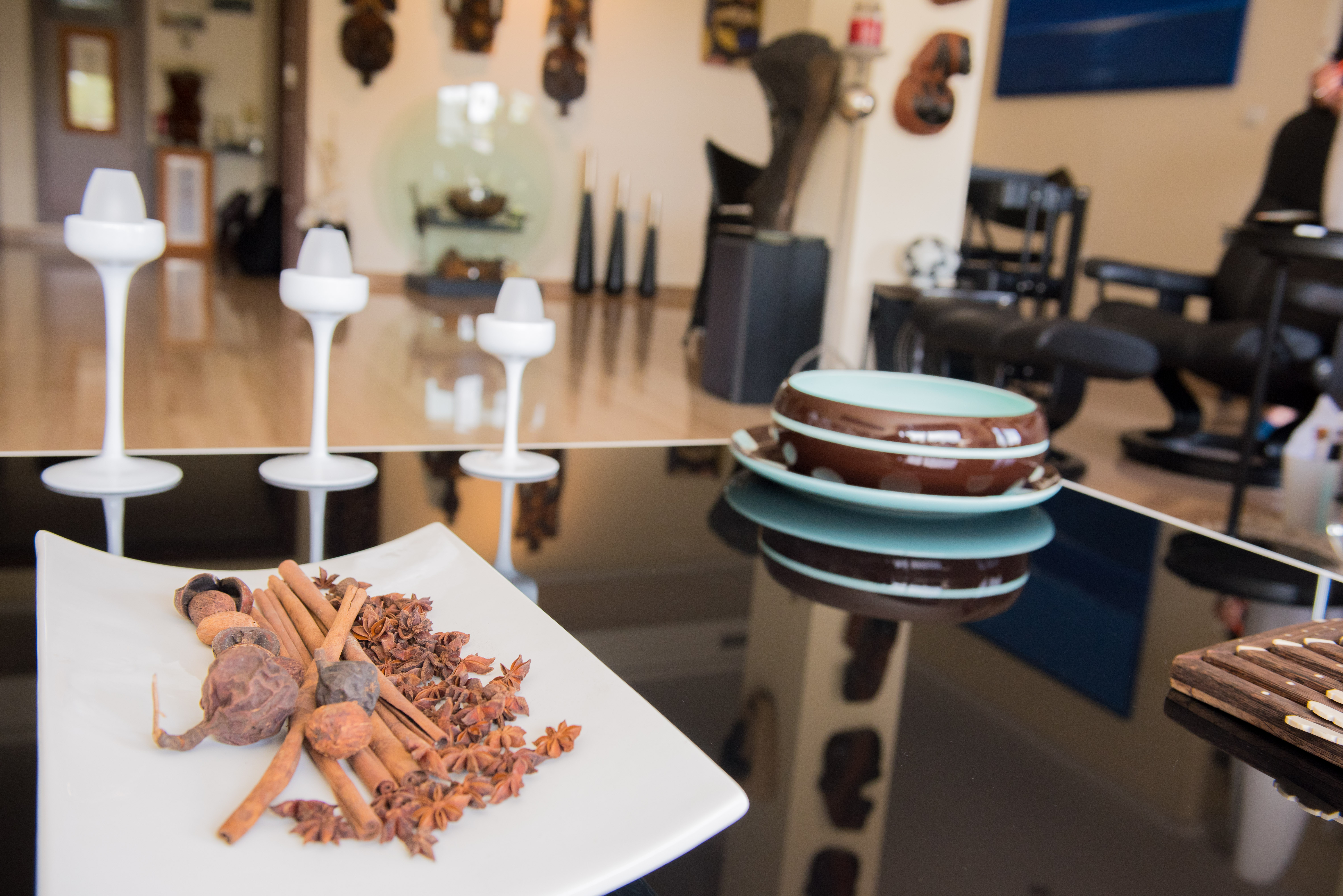 Detalle de una mesa reflectante con una bandeja de especias (canela, anís estrellado), modernos candelabros blancos y cuencos cerámicos. El fondo muestra un interior decorado. Detalle de una mesa reflectante con una bandeja de especias (canela, anís estrellado), modernos candelabros blancos y cuencos cerámicos. El fondo muestra un interior decorado.