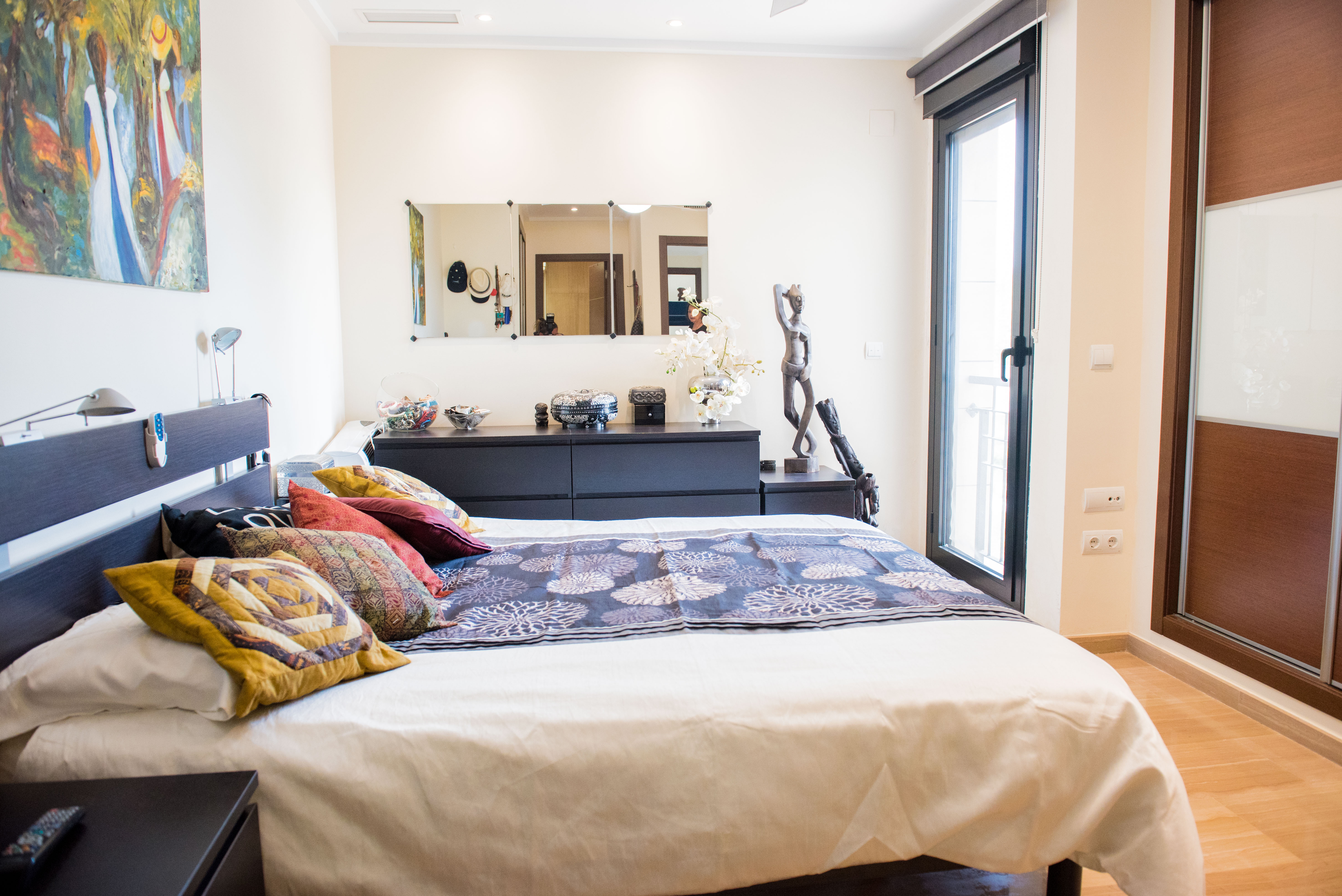 Dormitorio con mobiliario de madera oscura, armarios empotrados y ventanal con acceso al exterior. Incluye una cómoda con espejo y suelos de madera clara.