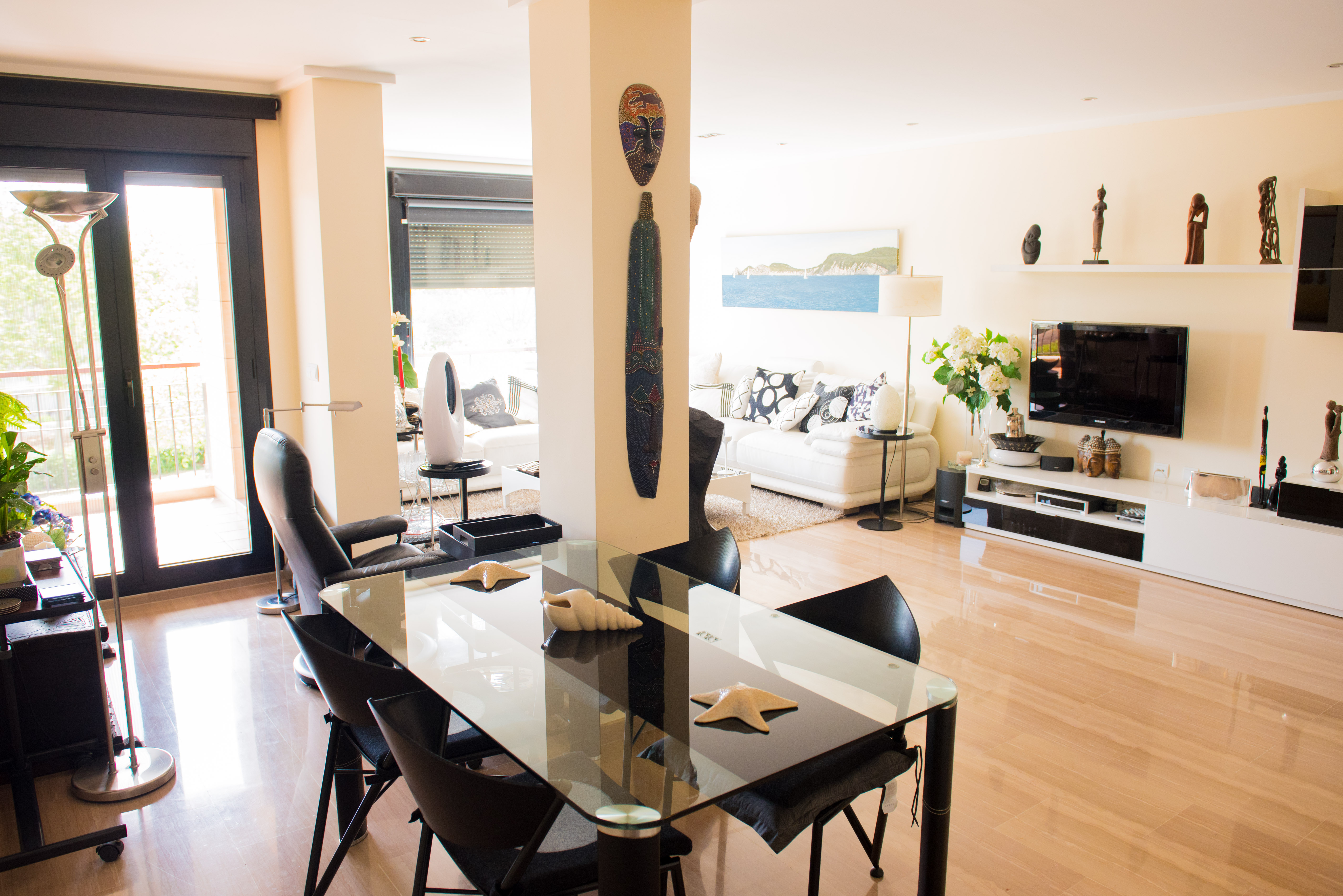 Salón-comedor luminoso con suelos de mármol pulido, mesa de cristal y acceso a la terraza. Decoración contemporánea con detalles étnicos y mobiliario en tonos neutros.