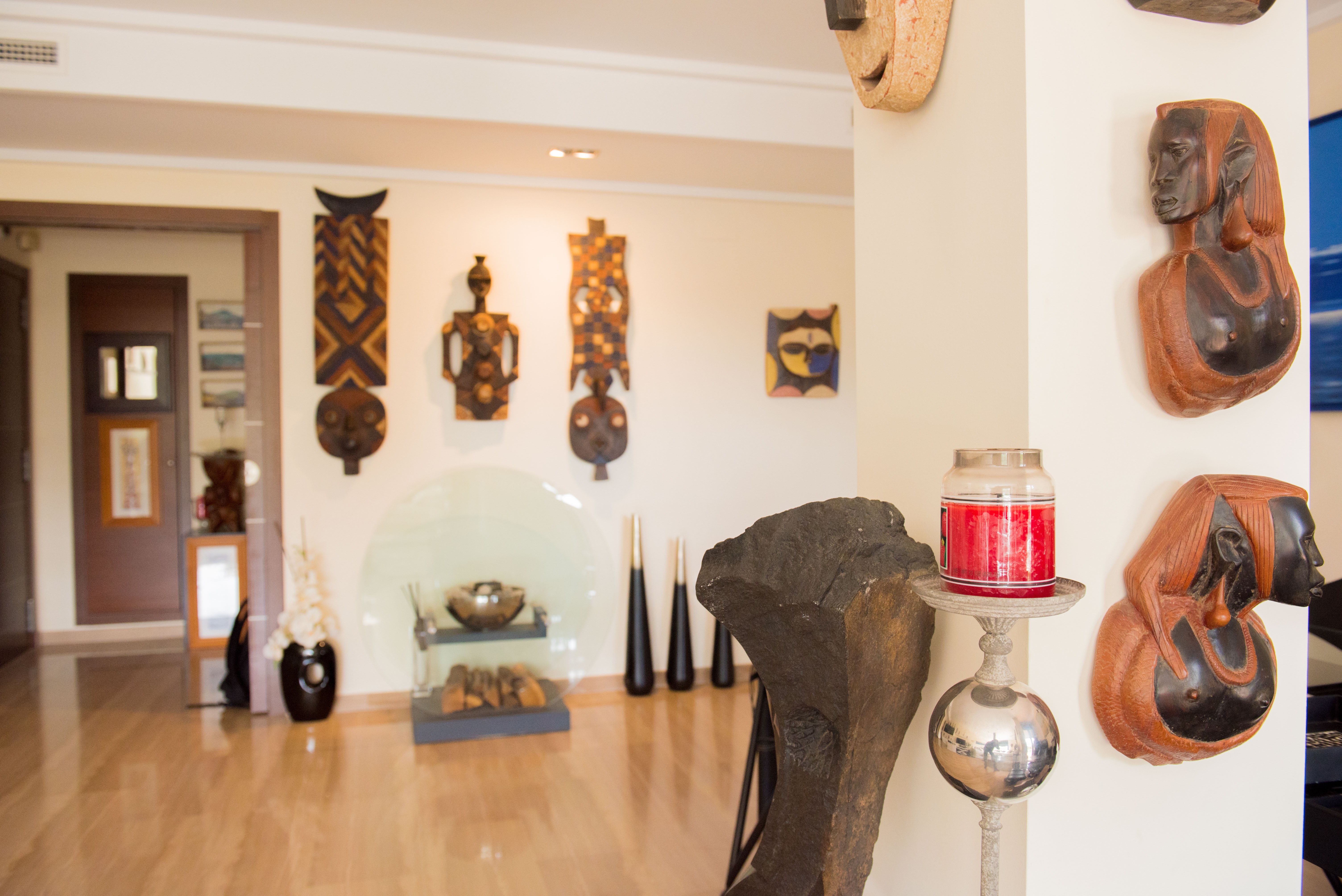 Un interior artístico que exhibe una colección curada de máscaras y bustos de madera tallada en paredes claras, complementado por un suelo de madera pulida y detalles decorativos modernos. Un interior artístico que exhibe una colección curada de máscaras y bustos de madera tallada en paredes claras, complementado por un suelo de madera pulida y detalles decorativos modernos.